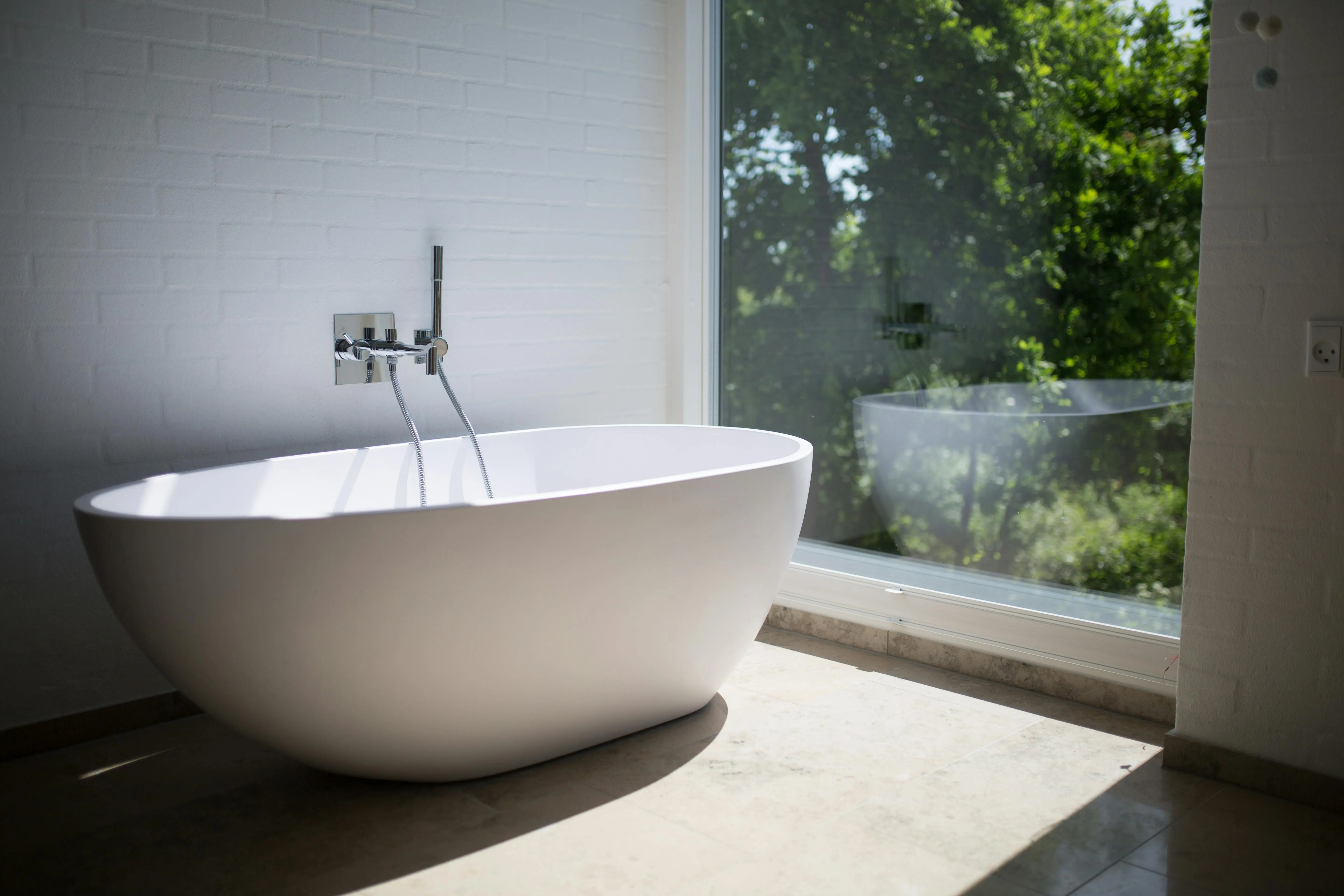 concrete bird bath Sleek white bathtub by large window in sunlit minimalist bathroom setting.