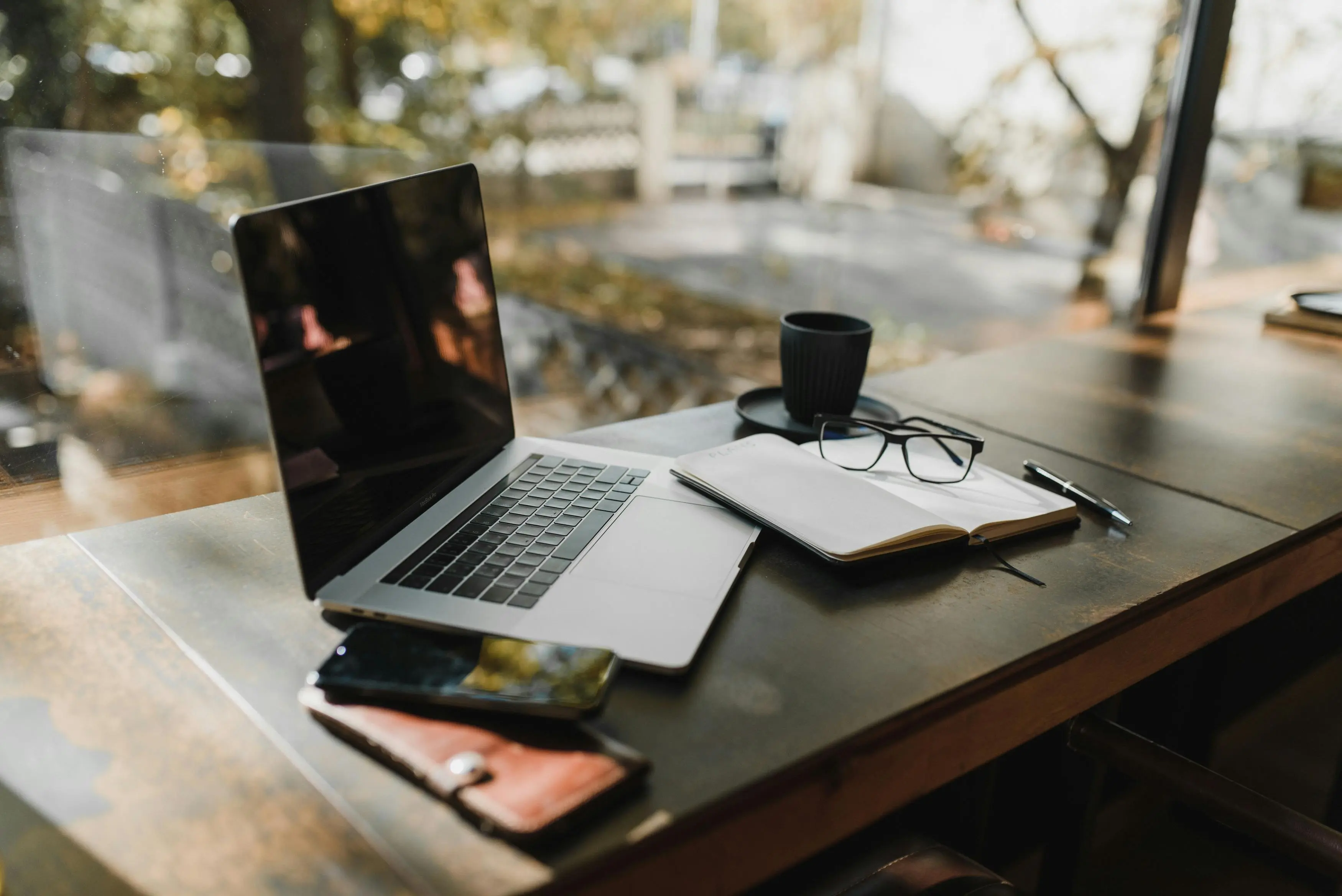 inexpensive team gifts A serene office setup with a laptop, notebook, and coffee near a window, reflecting an autumn scene.