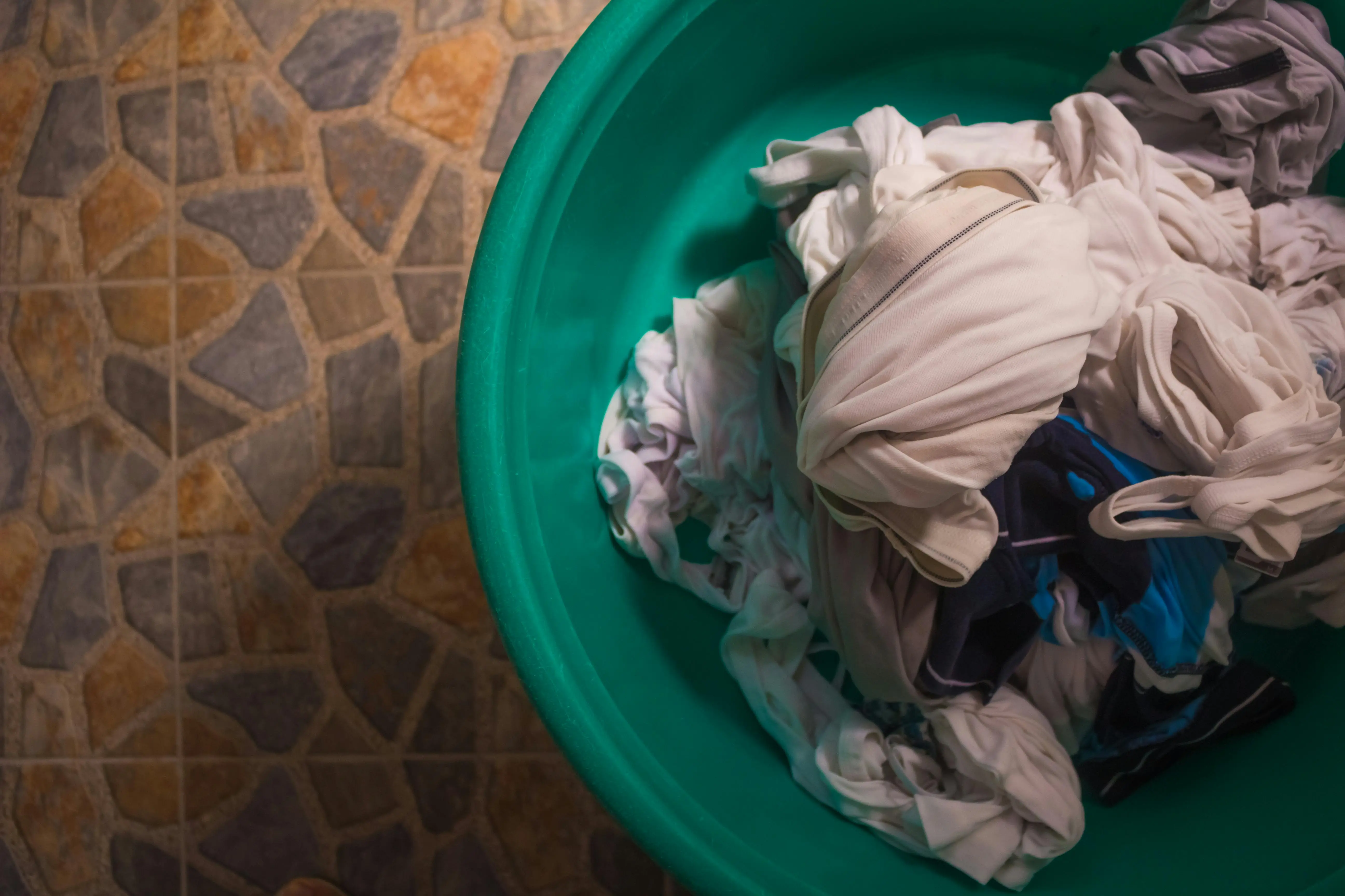 what might protect your shirt from a grease stain Top view of a laundry basket filled with crumpled clothes on a tiled floor.