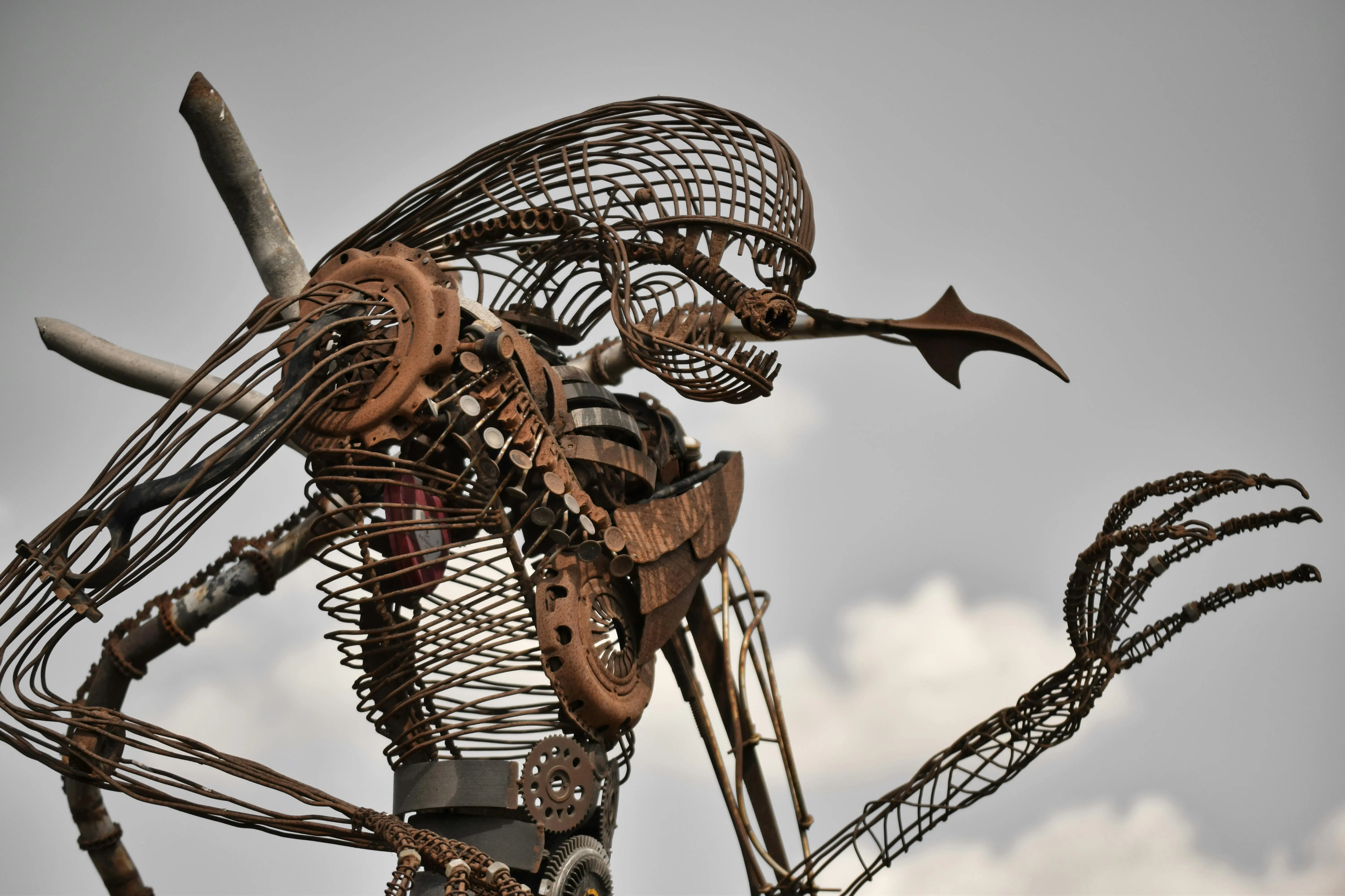 wrought iron patio furniture An intricately designed metal sculpture crafted from rusted wire and gears against a clear sky.