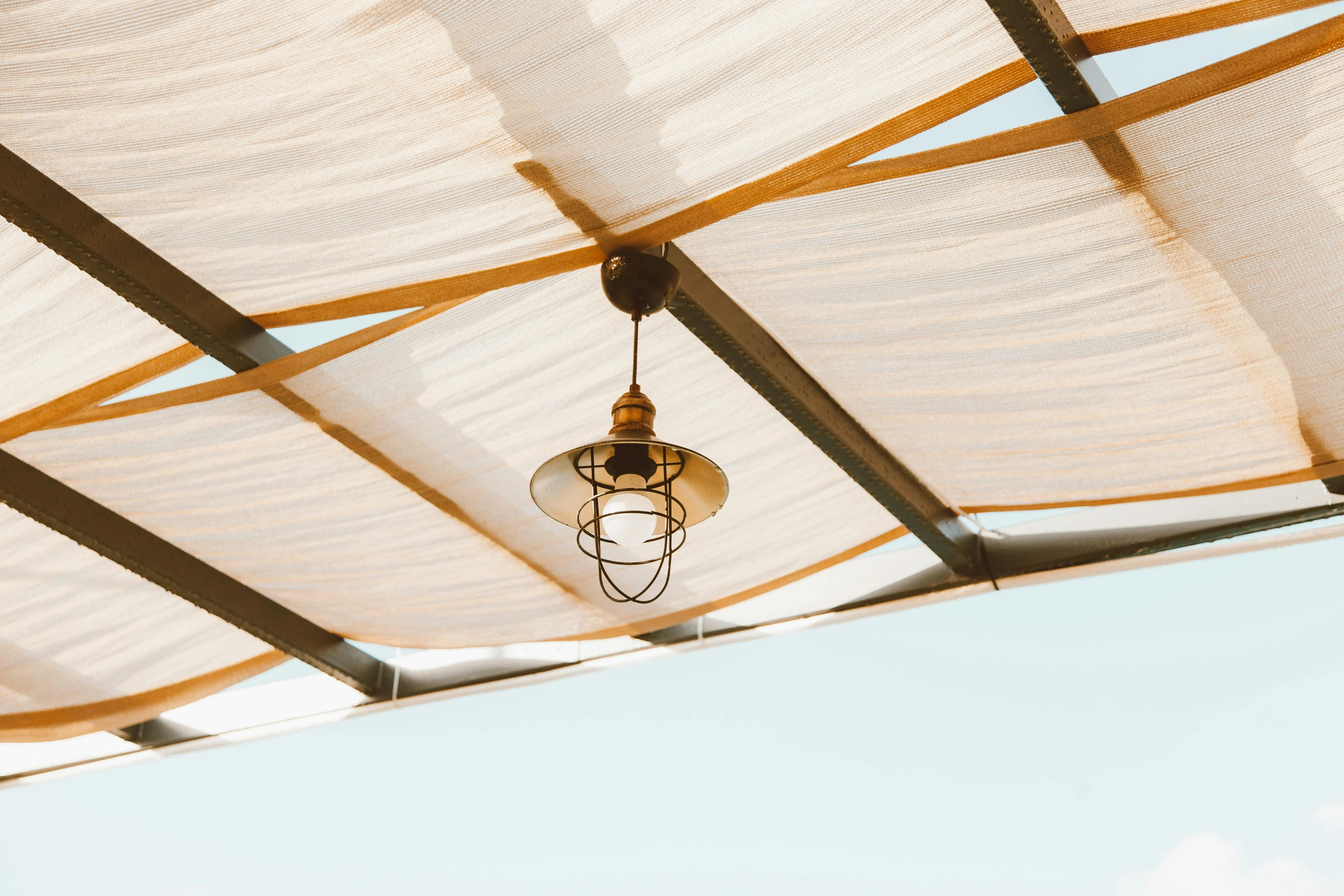 plants for lots of sun Minimalist industrial lamp hanging under a fabric ceiling against a clear blue sky.