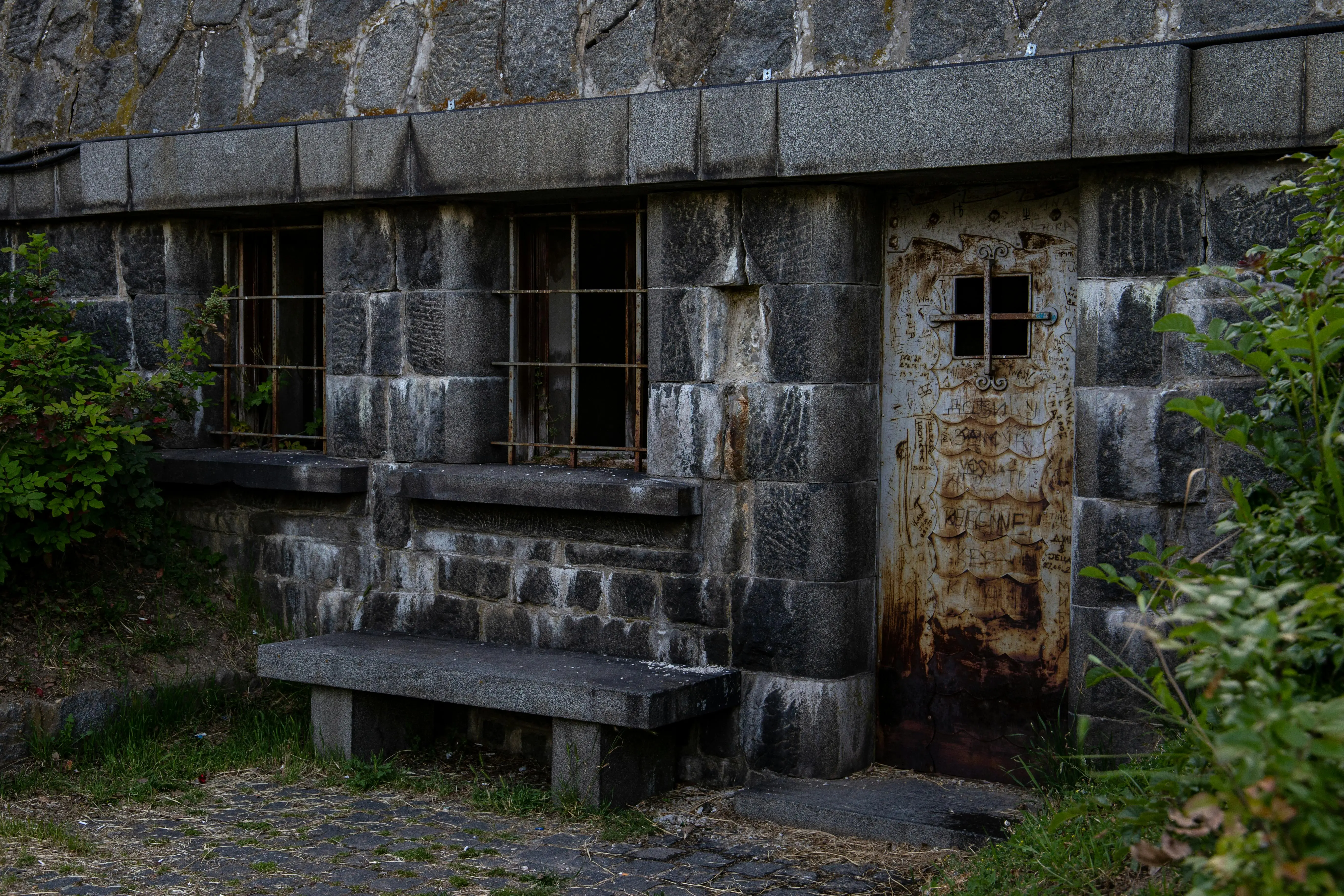wrought iron patio furniture Abandoned stone building with rusty door and barred windows, overgrown with plants.