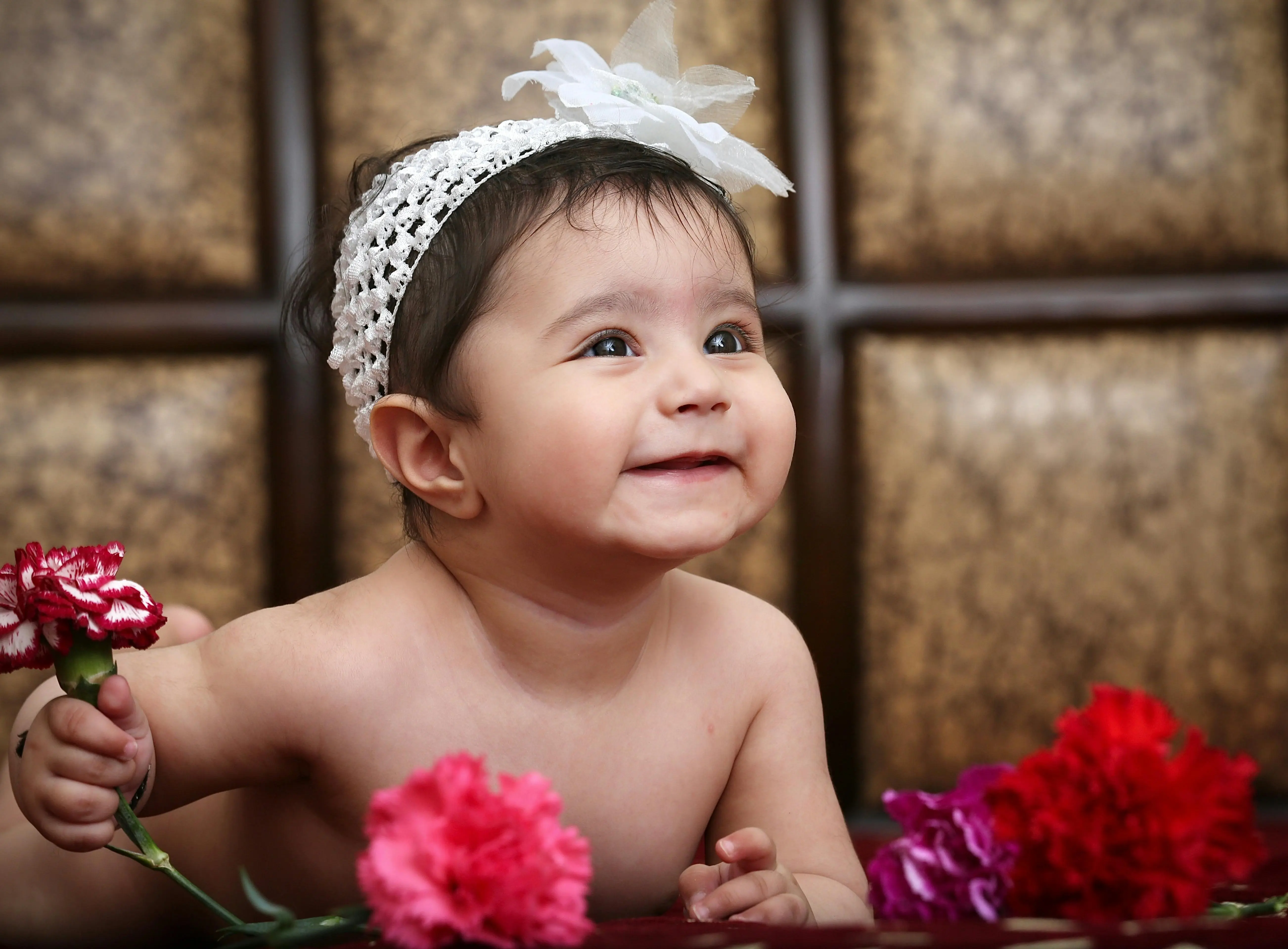 pink carnations Adorable baby smiling while holding carnations, wearing a white headband indoors.