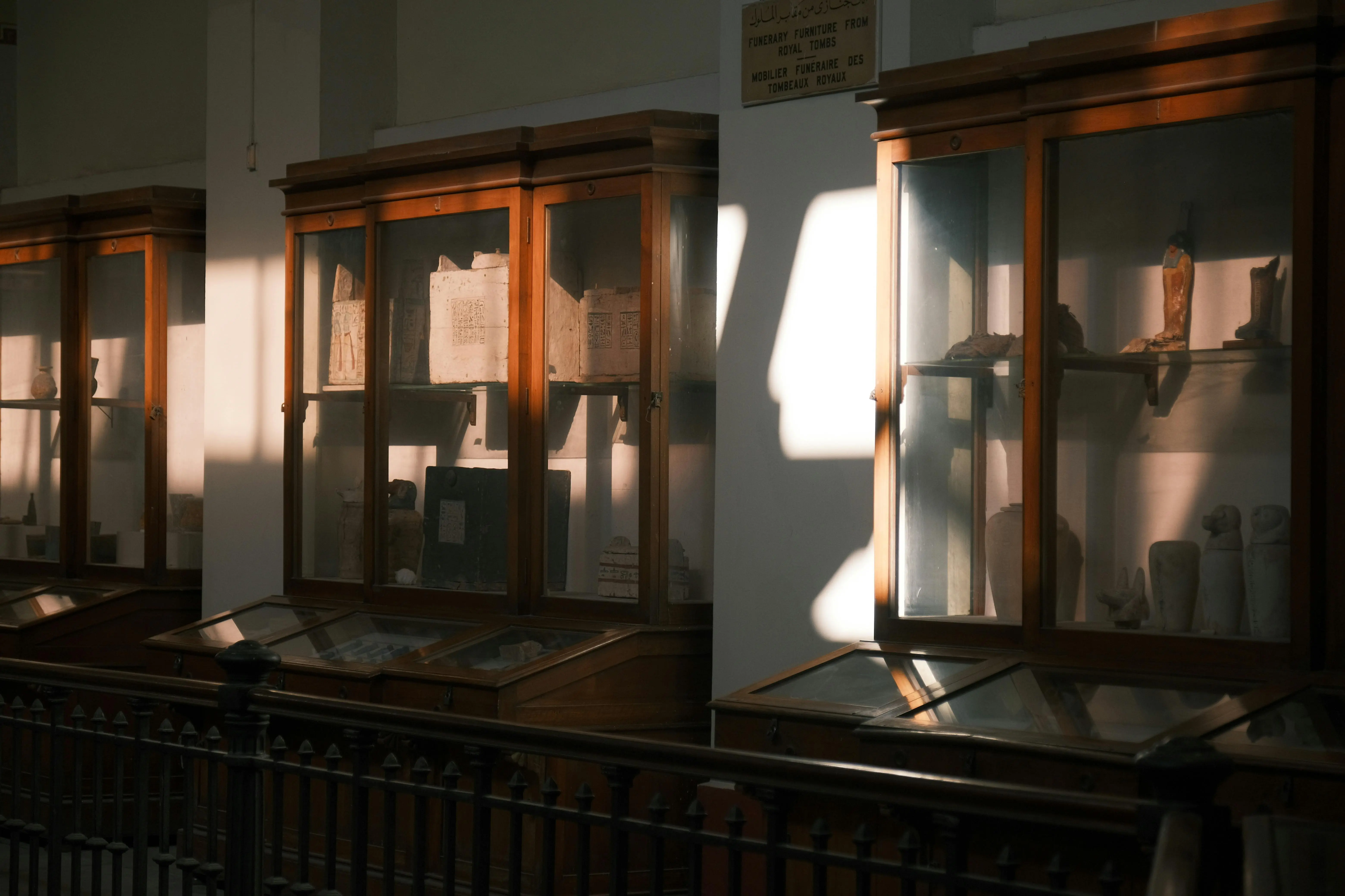 glass cabinet doors Antique display cabinets in a museum, illuminated by warm sunlight.