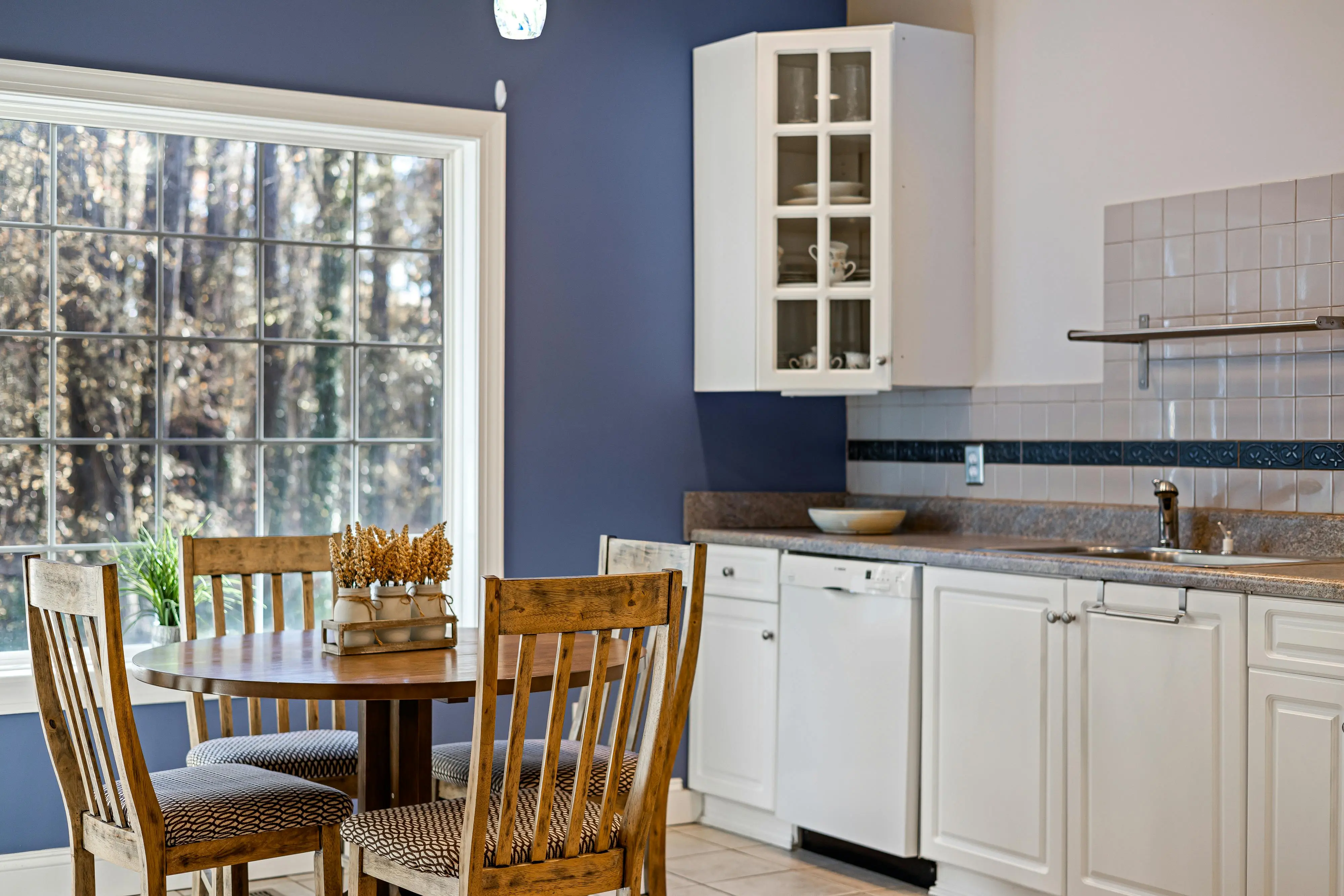 glass cabinet doors A bright kitchen with a round wooden dining table, white cabinets, and large window.