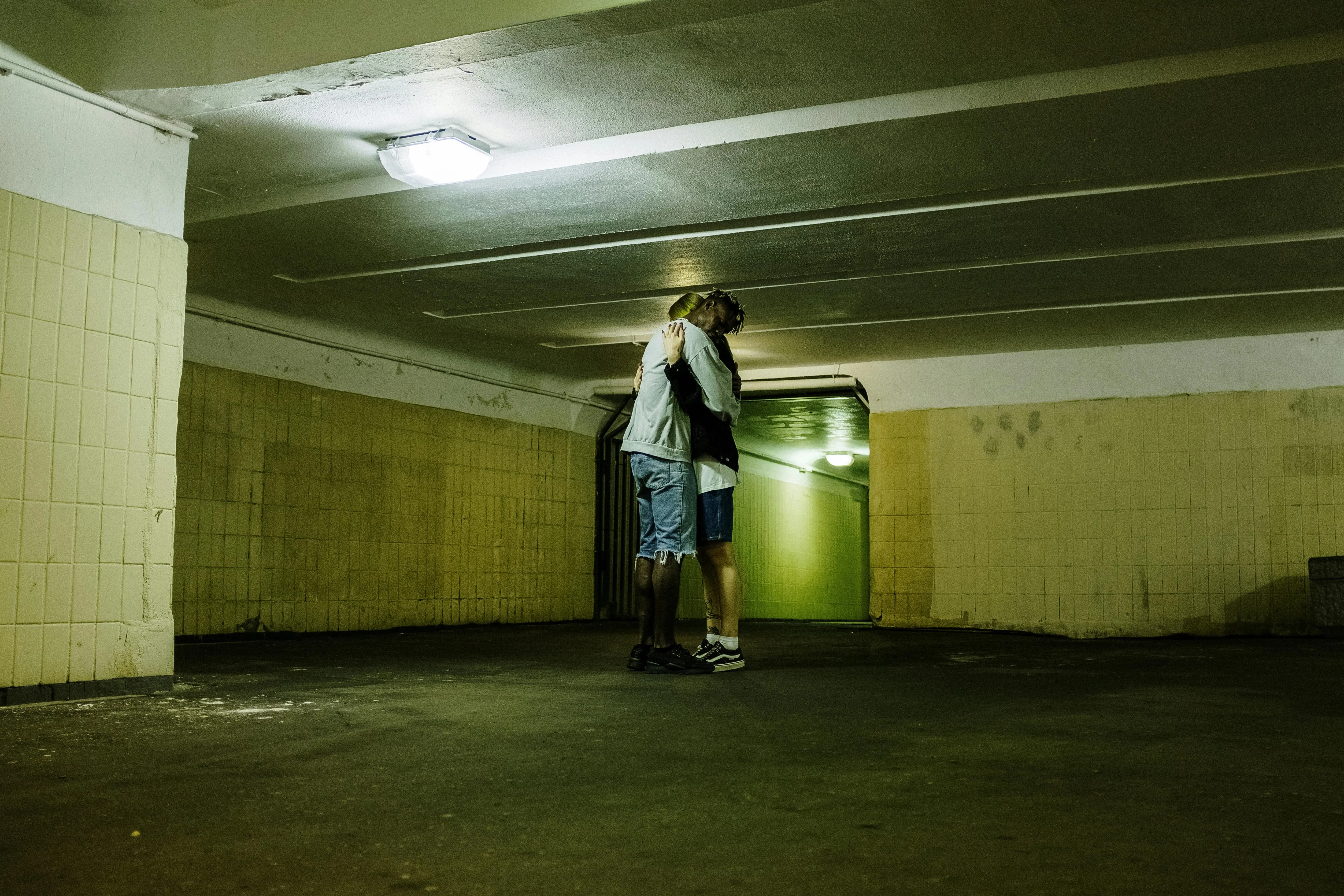 green tile Couple embracing under a fluorescent light in an underground urban passage.