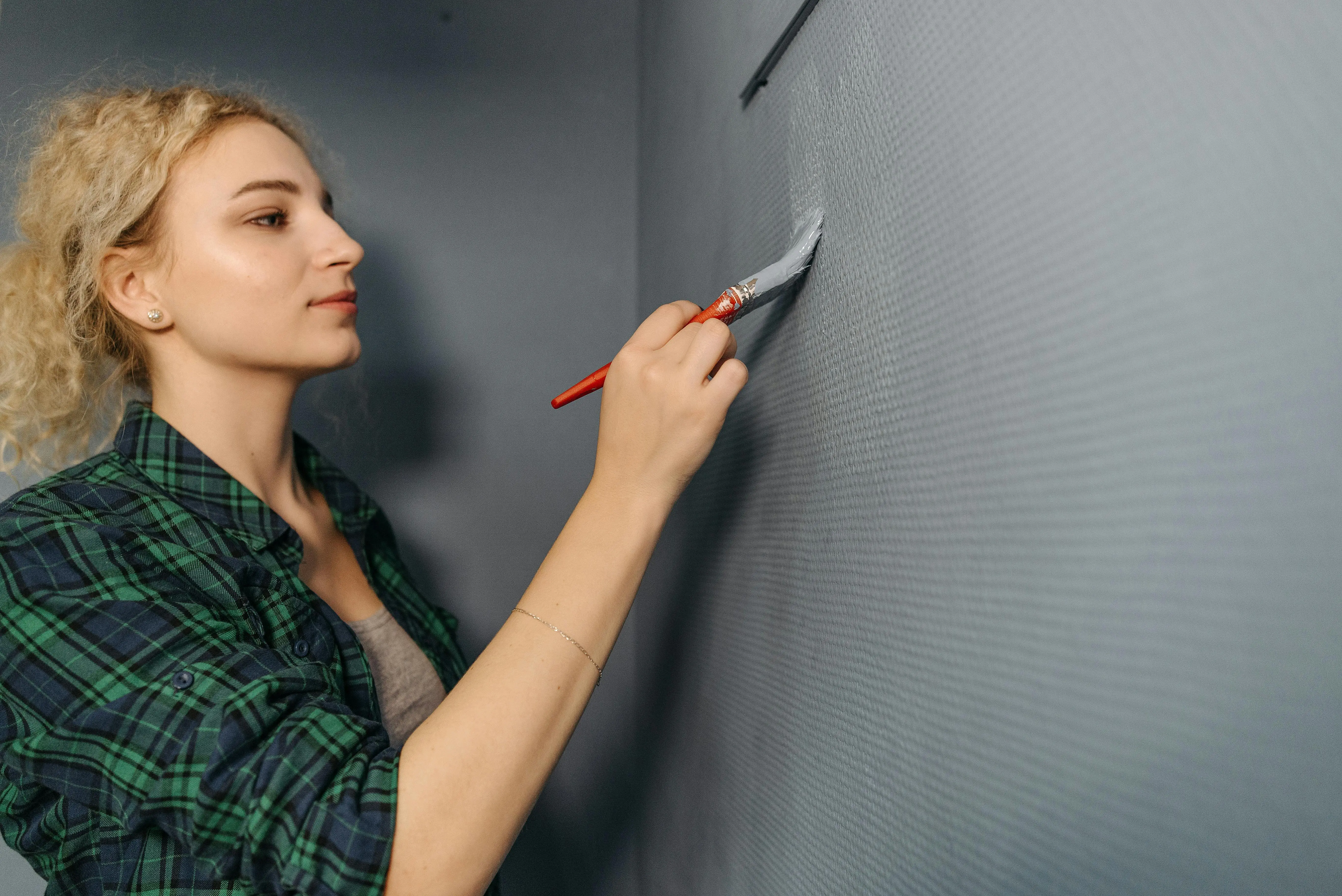 grey paint A woman in a plaid shirt painting a gray wall indoors, focusing on home improvement.