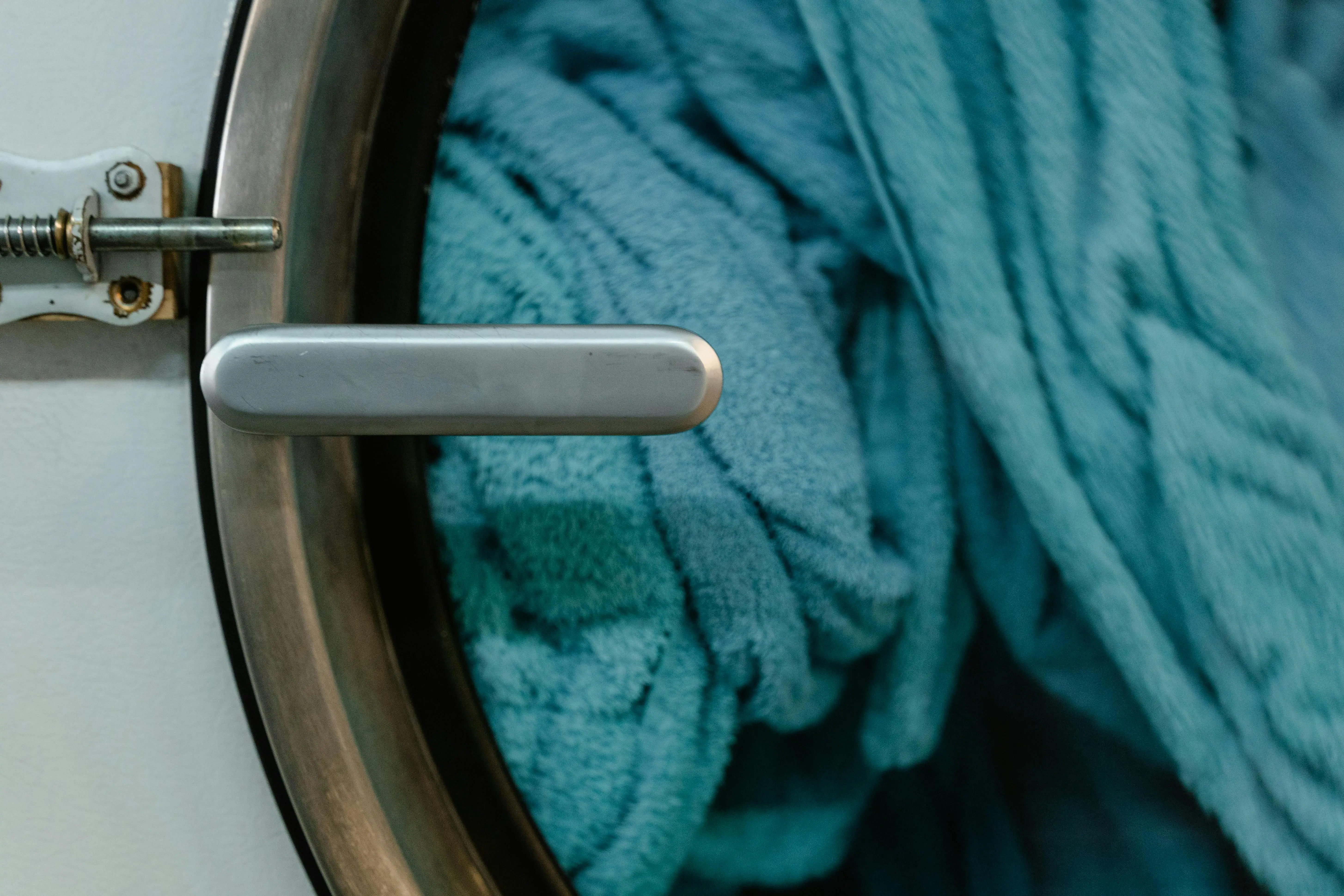 how to get mildew smell out of clothes Detailed image of a washing machine door with blue towels inside, focusing on household chores.