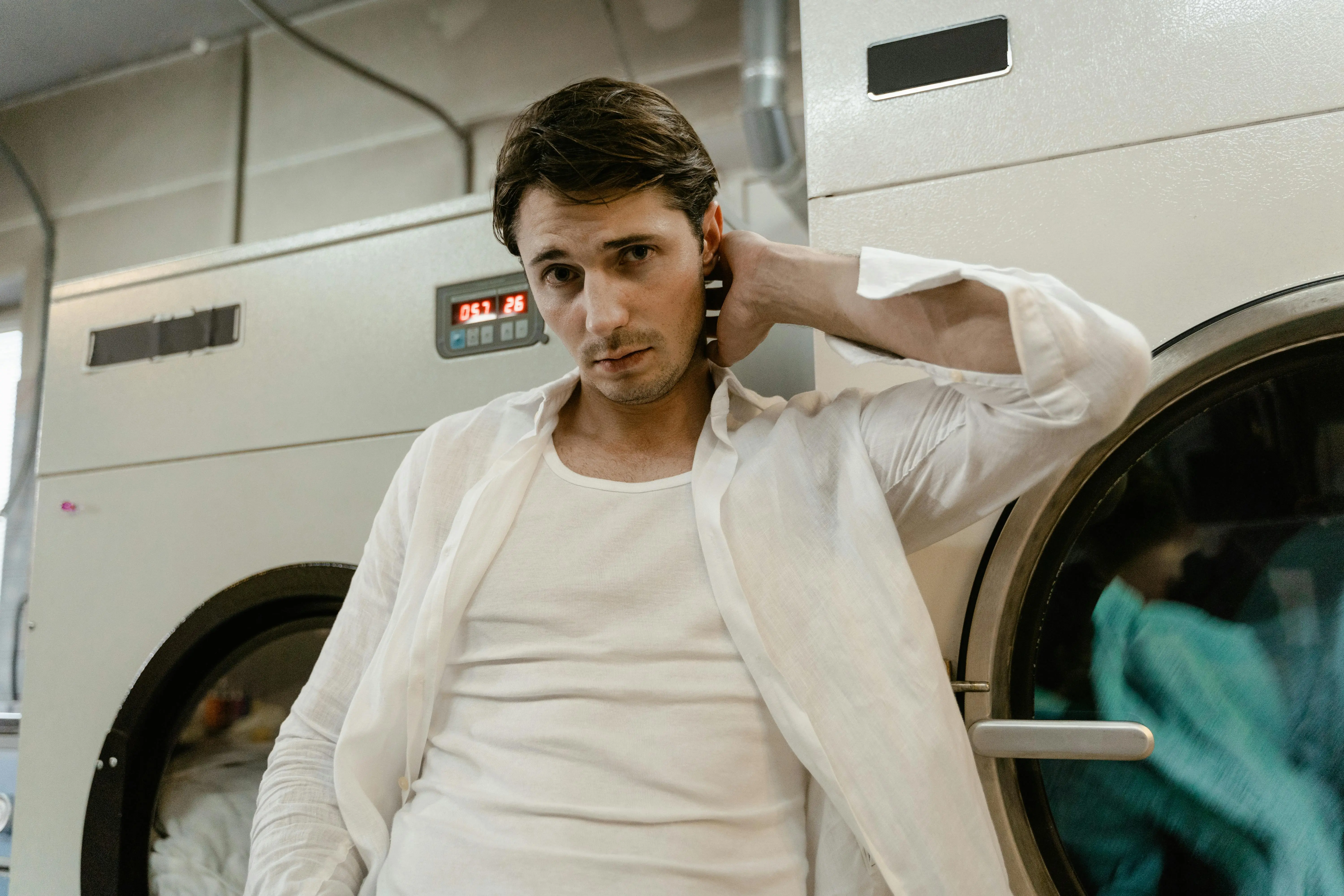 commercial washing machine Young man in a white shirt leaning on a washing machine in a laundry facility.