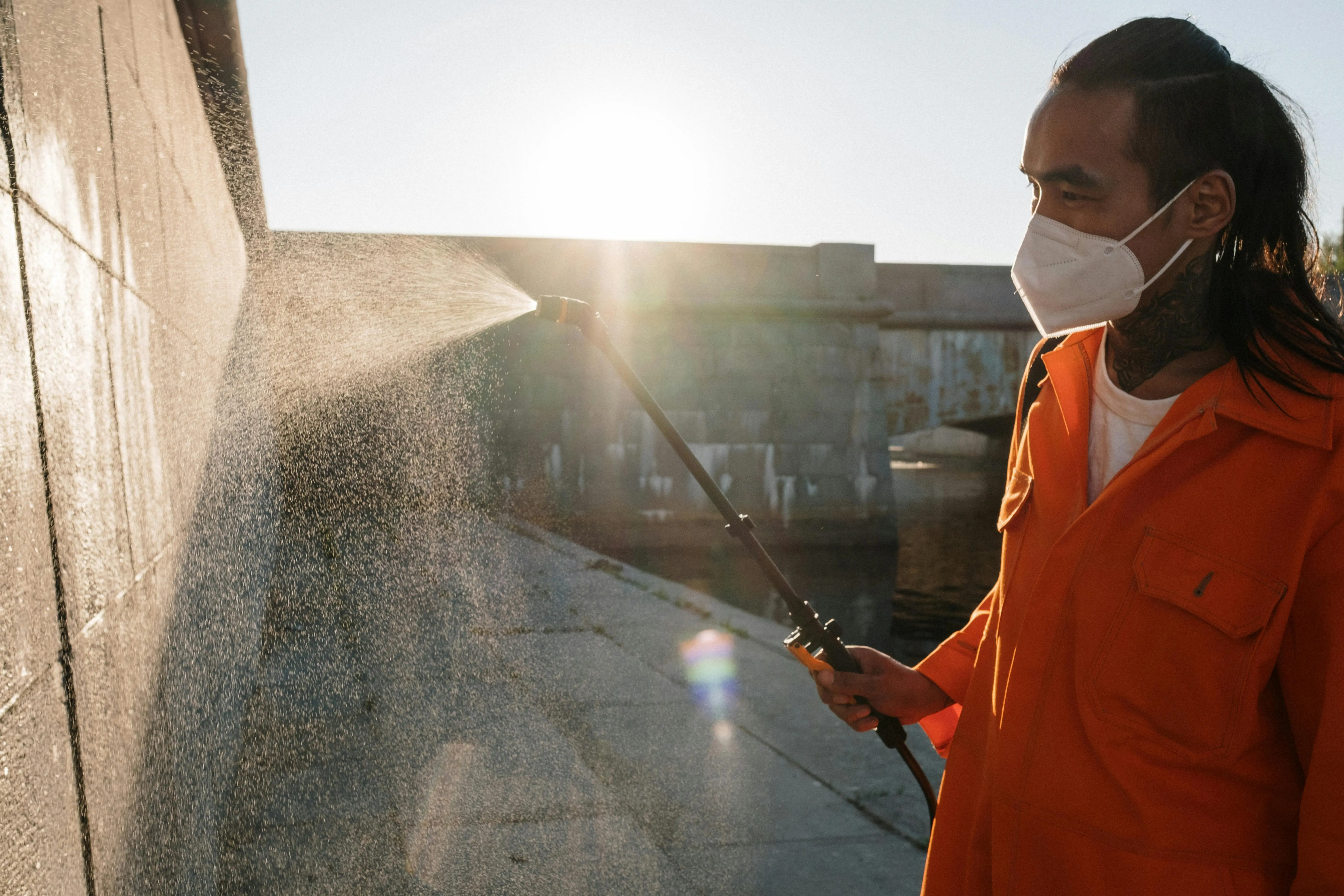 rat poop vs mouse poop Man in orange uniform wearing facemask sprays water on wall outdoors, sunlight shining.