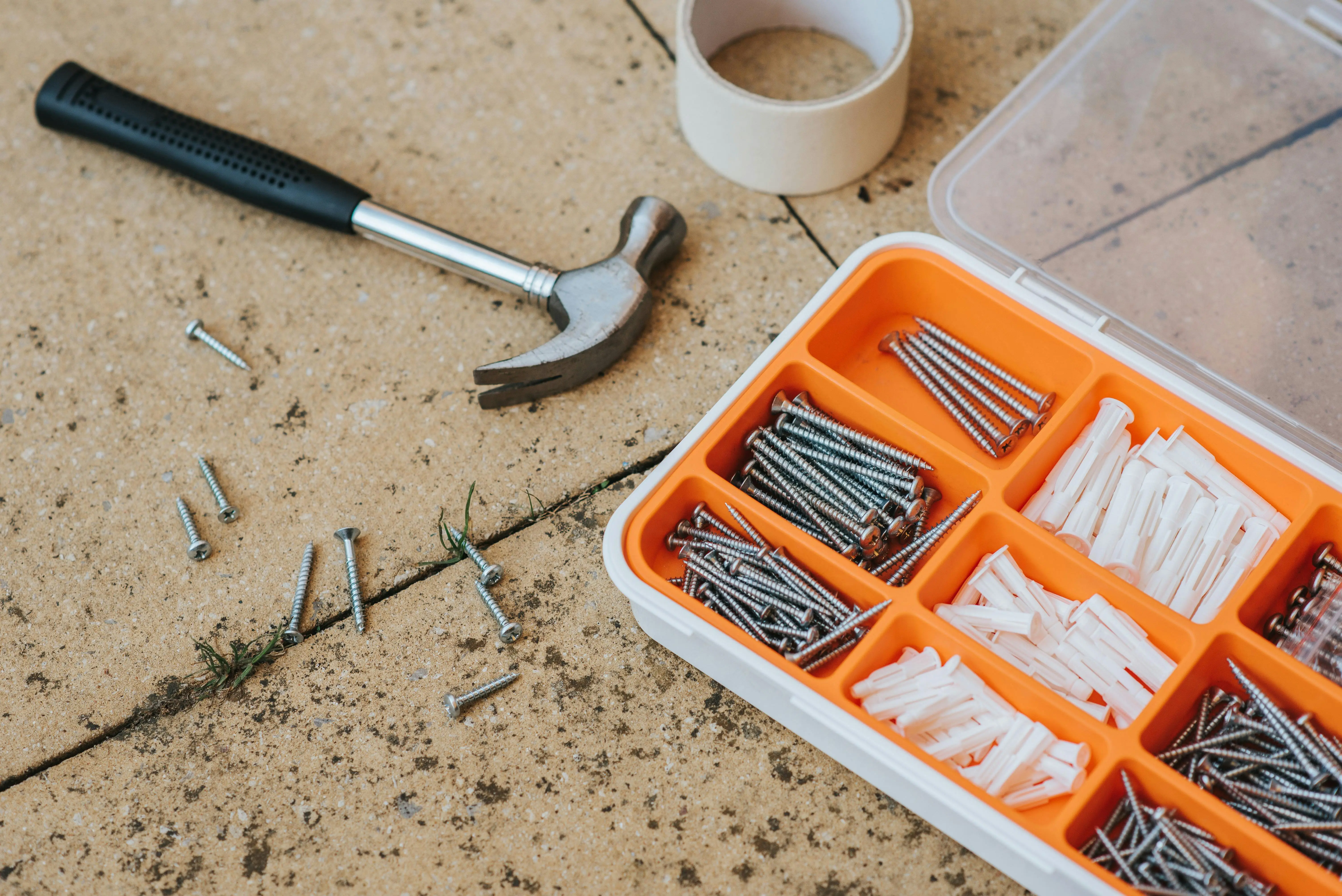 diy tool box Overhead view of a toolkit with a hammer, screws, and anchors on a concrete surface.