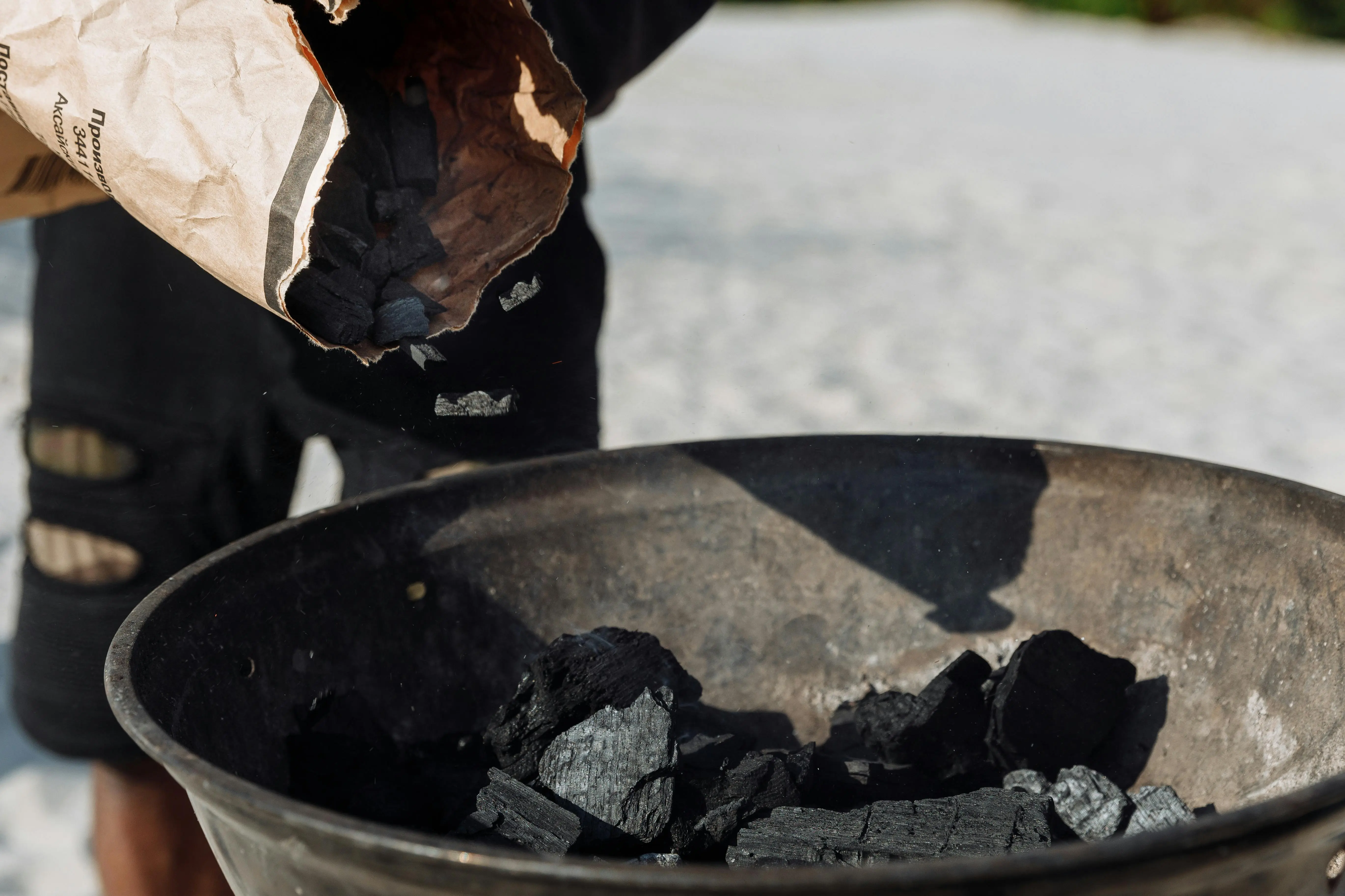 how to get smoke smell out of clothes Detailed image of charcoal poured from a bag into a grilling basin outdoors.