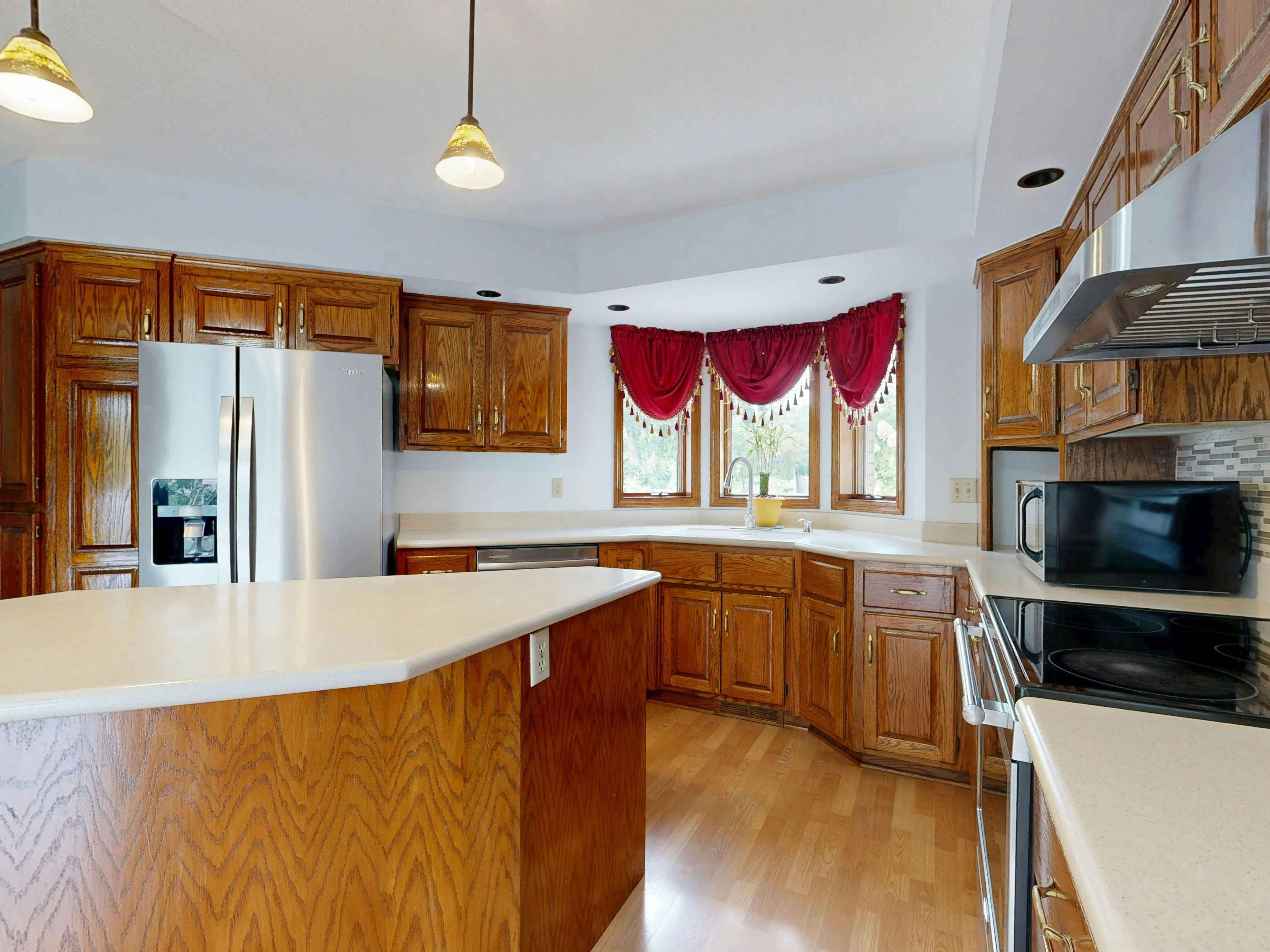 oak cabinet A bright, modern kitchen featuring wooden cabinets, island, and stainless steel appliances.