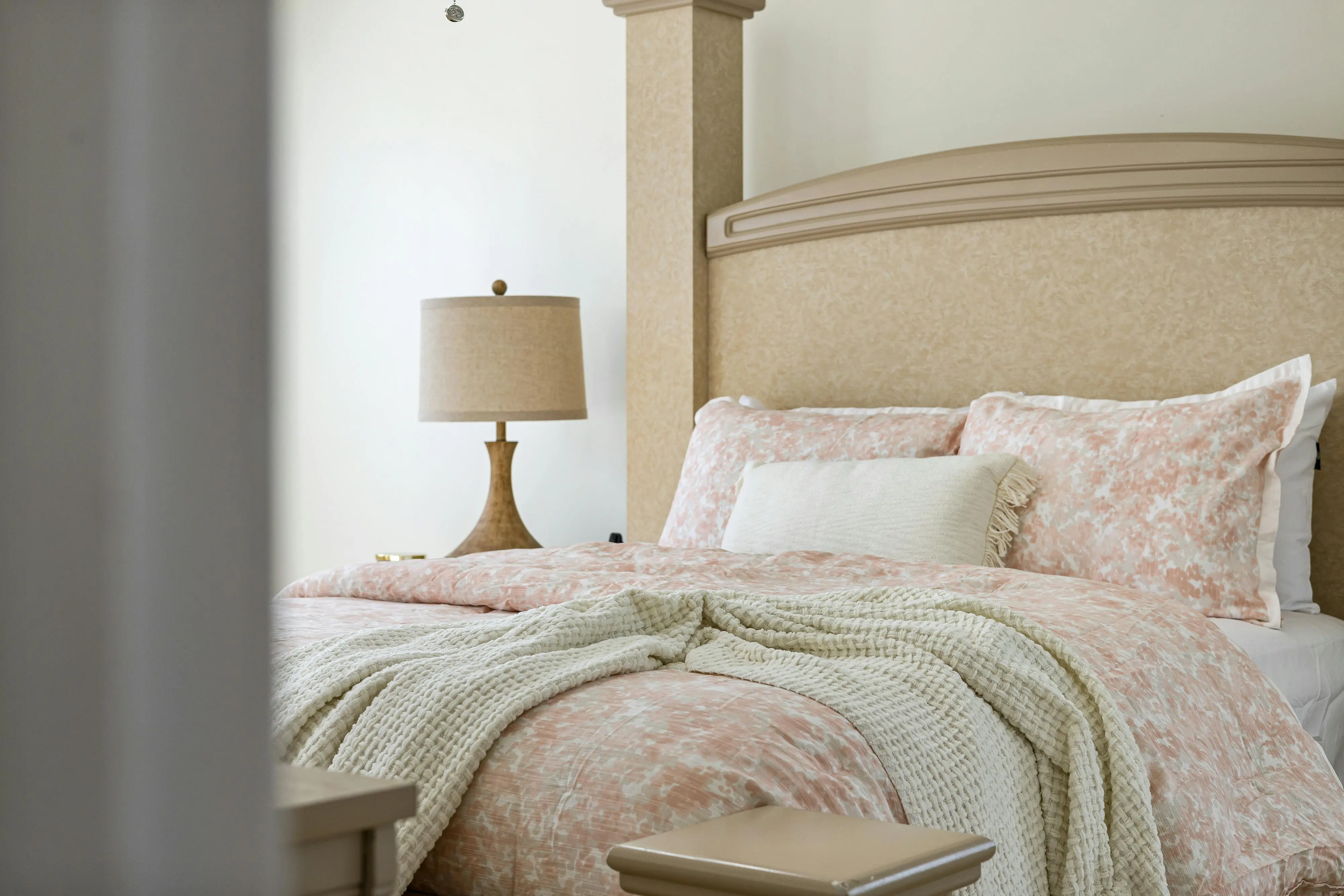 corner bed design Inviting bedroom with soft pink bedding, knitted blanket, and elegant lamp.