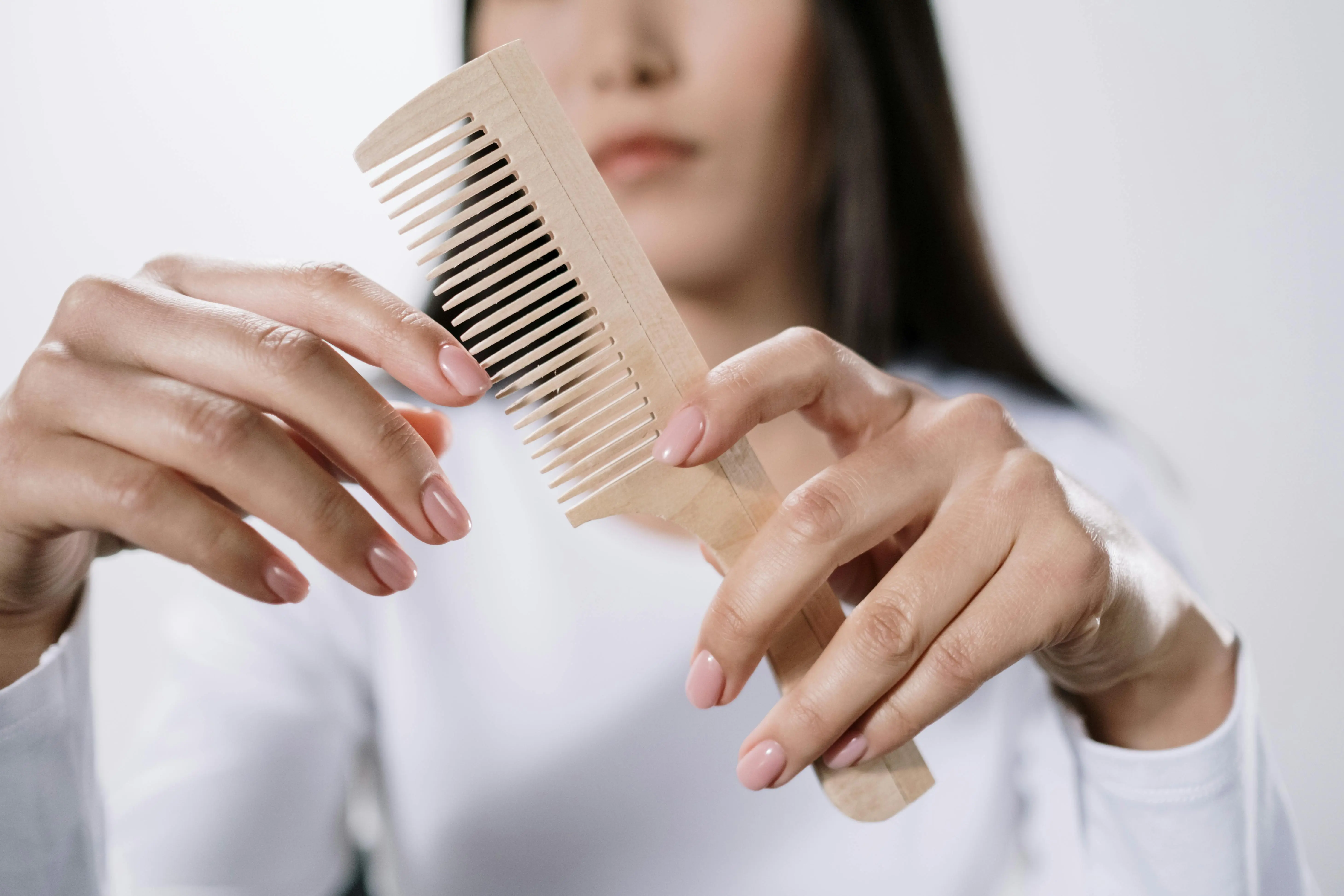 how to get blood out of jeans A woman holding a wooden comb with focus on her hands and the comb, promoting natural grooming.