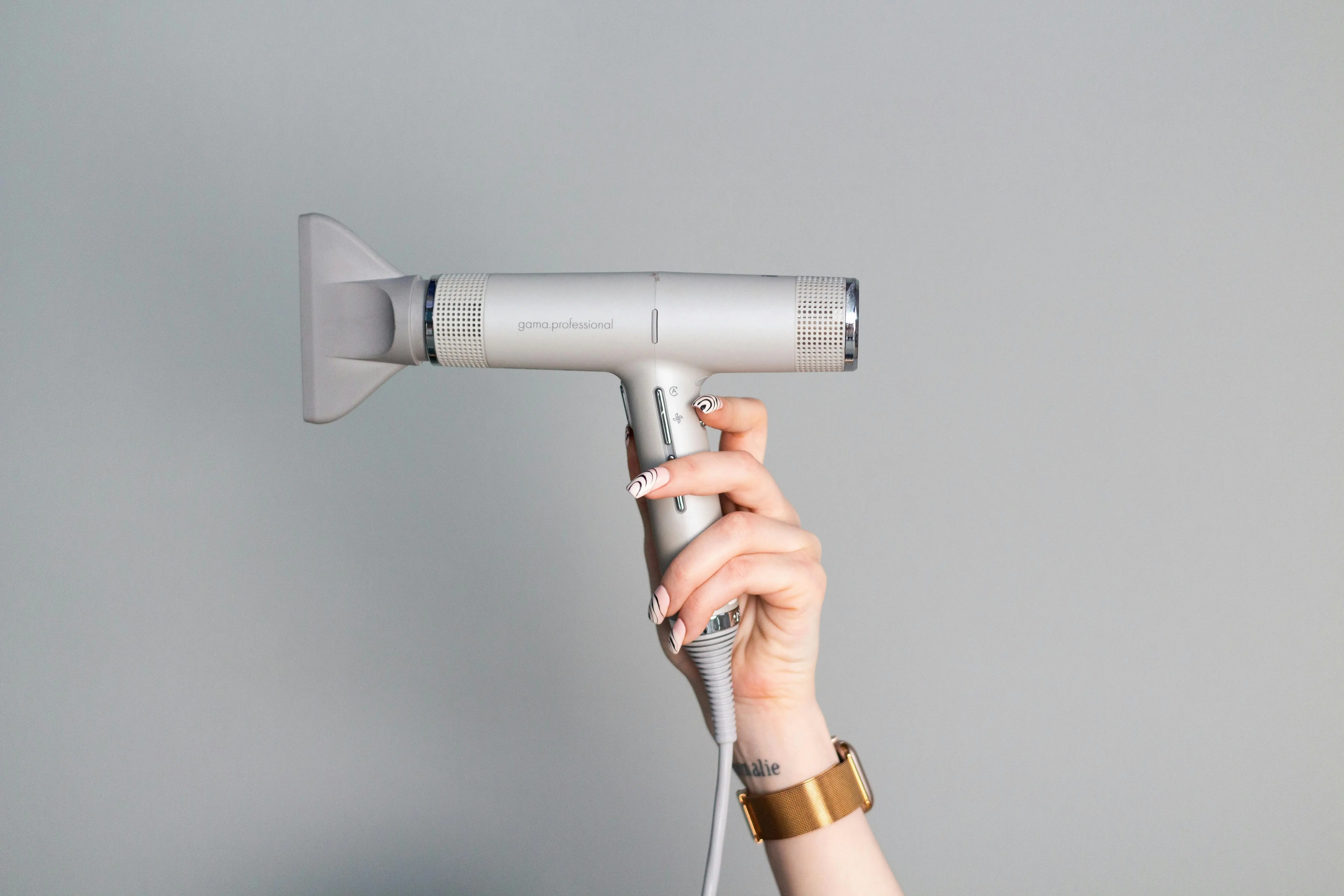 how to get rid of static electricity A close-up of a hand with manicured nails holding a sleek hair dryer against a neutral background.