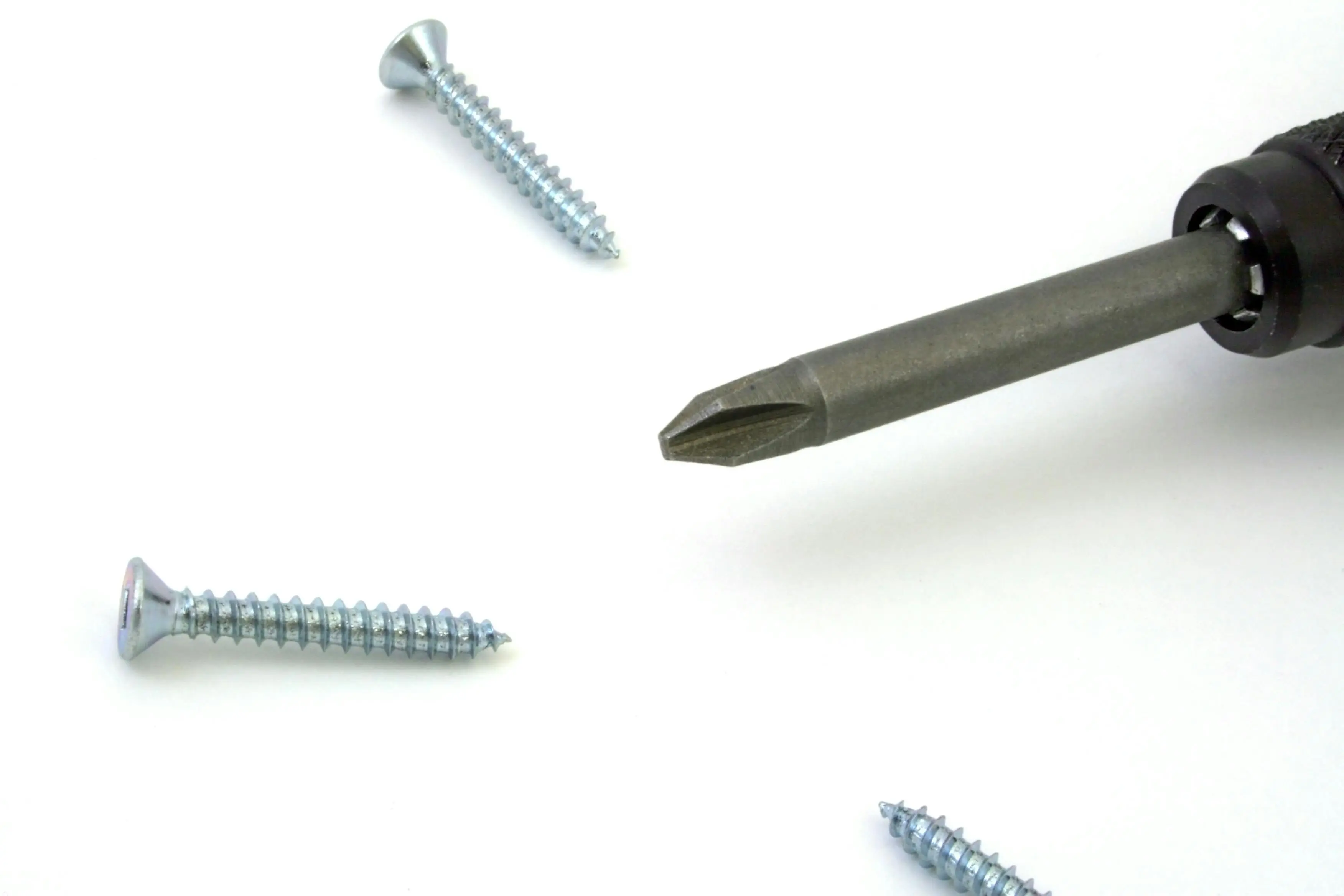 drywall screw dimensions A detailed view of a screwdriver with screws scattered on a white surface, ideal for tool or maintenance themes.