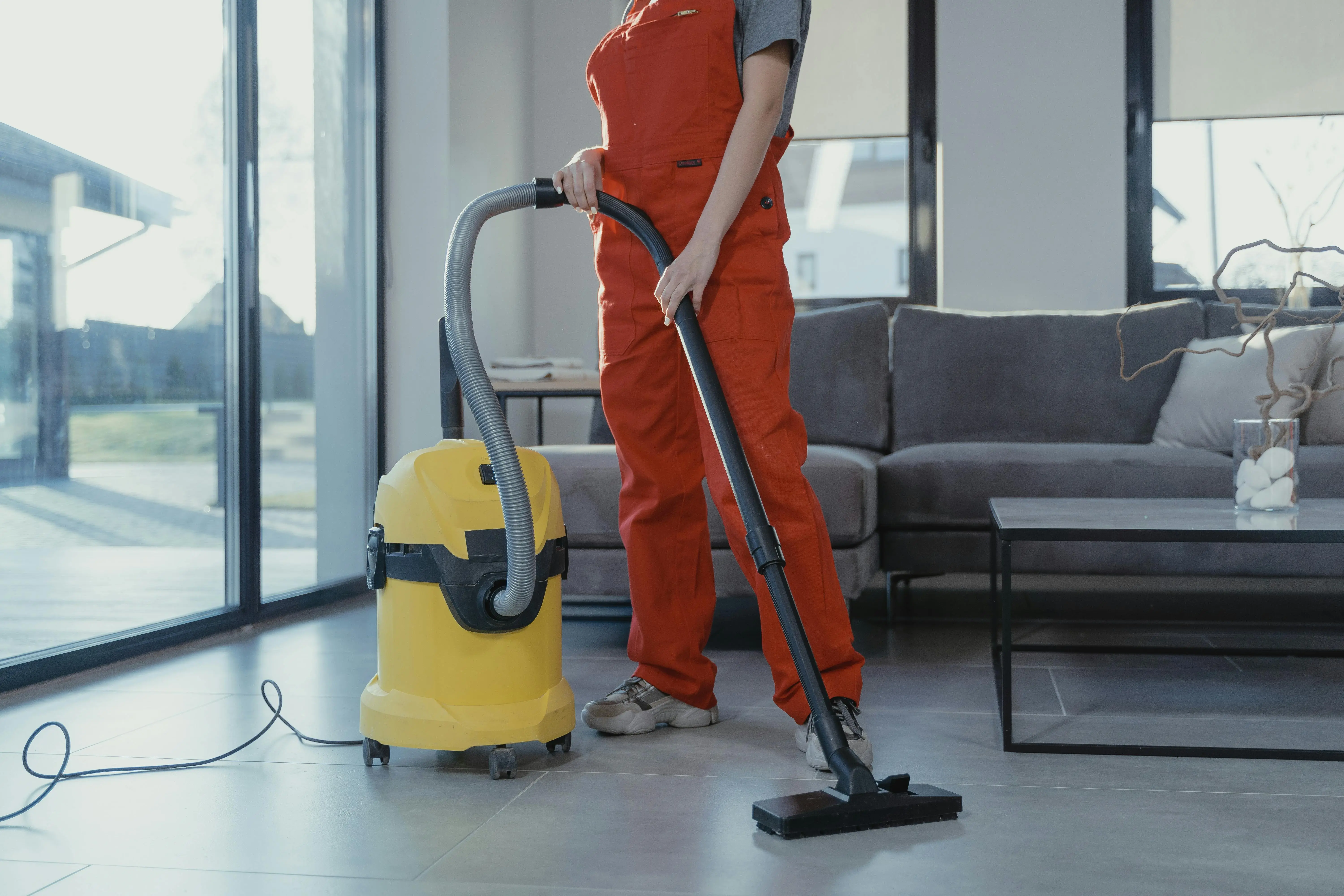 how to get smoke smell out of clothes A professional cleaner in red coveralls vacuuming a modern living room with a yellow vacuum cleaner.