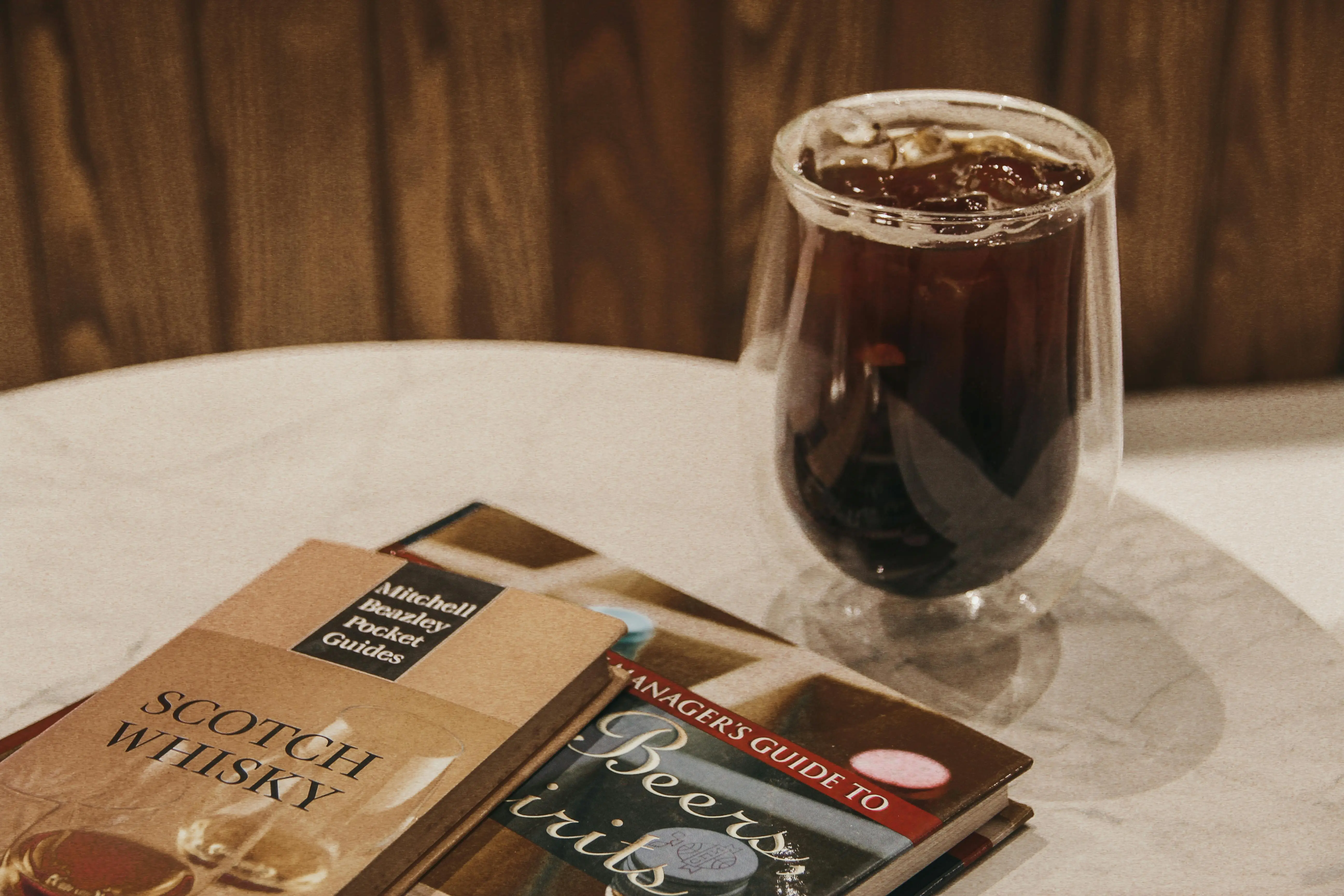 lift top cocktail table A refreshing glass of iced coffee beside books on whisky and beer for a cozy reading time.