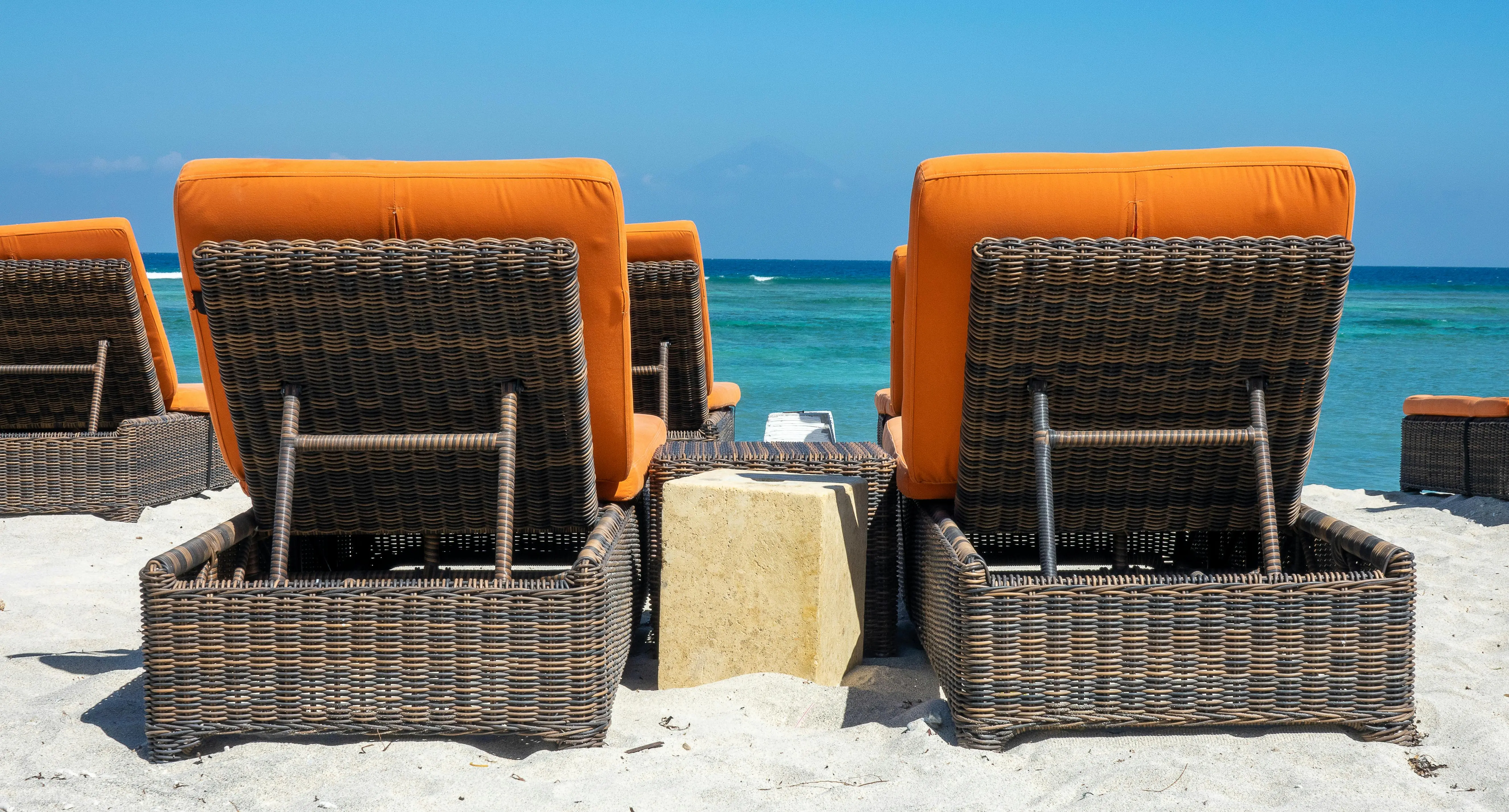 coastal decorative pillows Wicker lounge chairs with orange cushions facing the sea on a sunny beach.