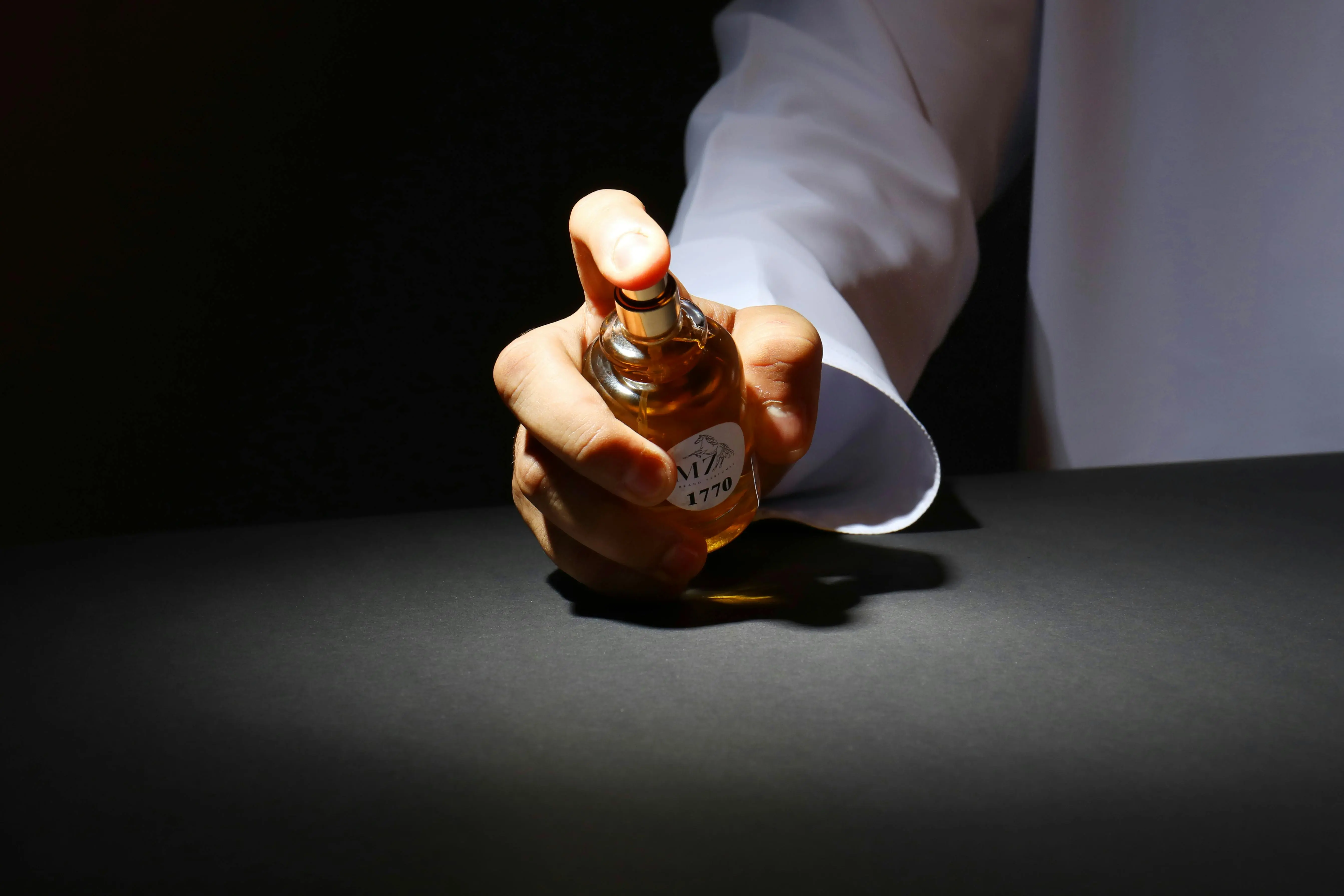 how to get pee smell out of clothes A hand elegantly holding a perfume bottle against a dark backdrop, highlighting luxury fragrance.