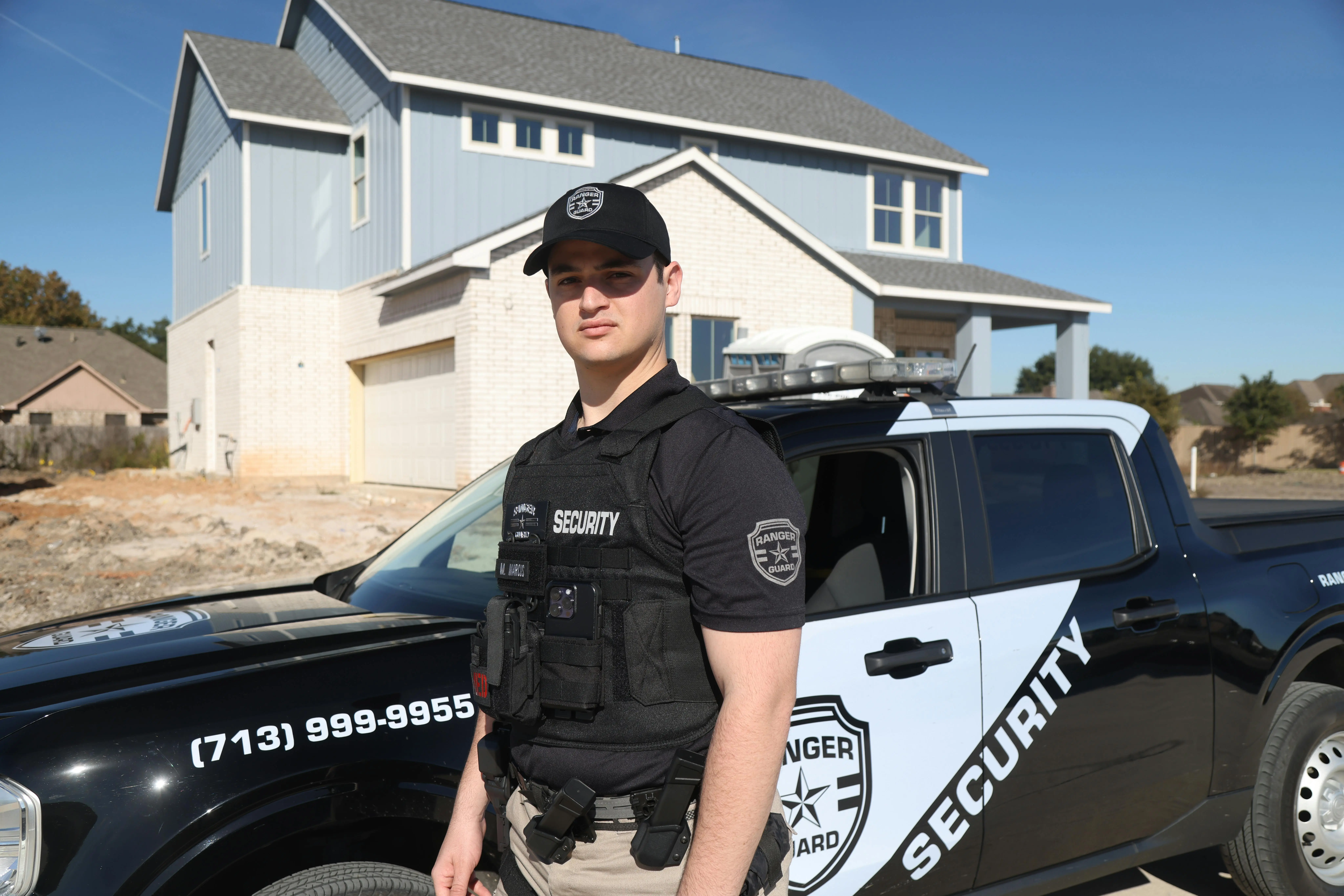 led outdoor spotlights Security guard in uniform stands beside patrol car outside residential building in daylight.