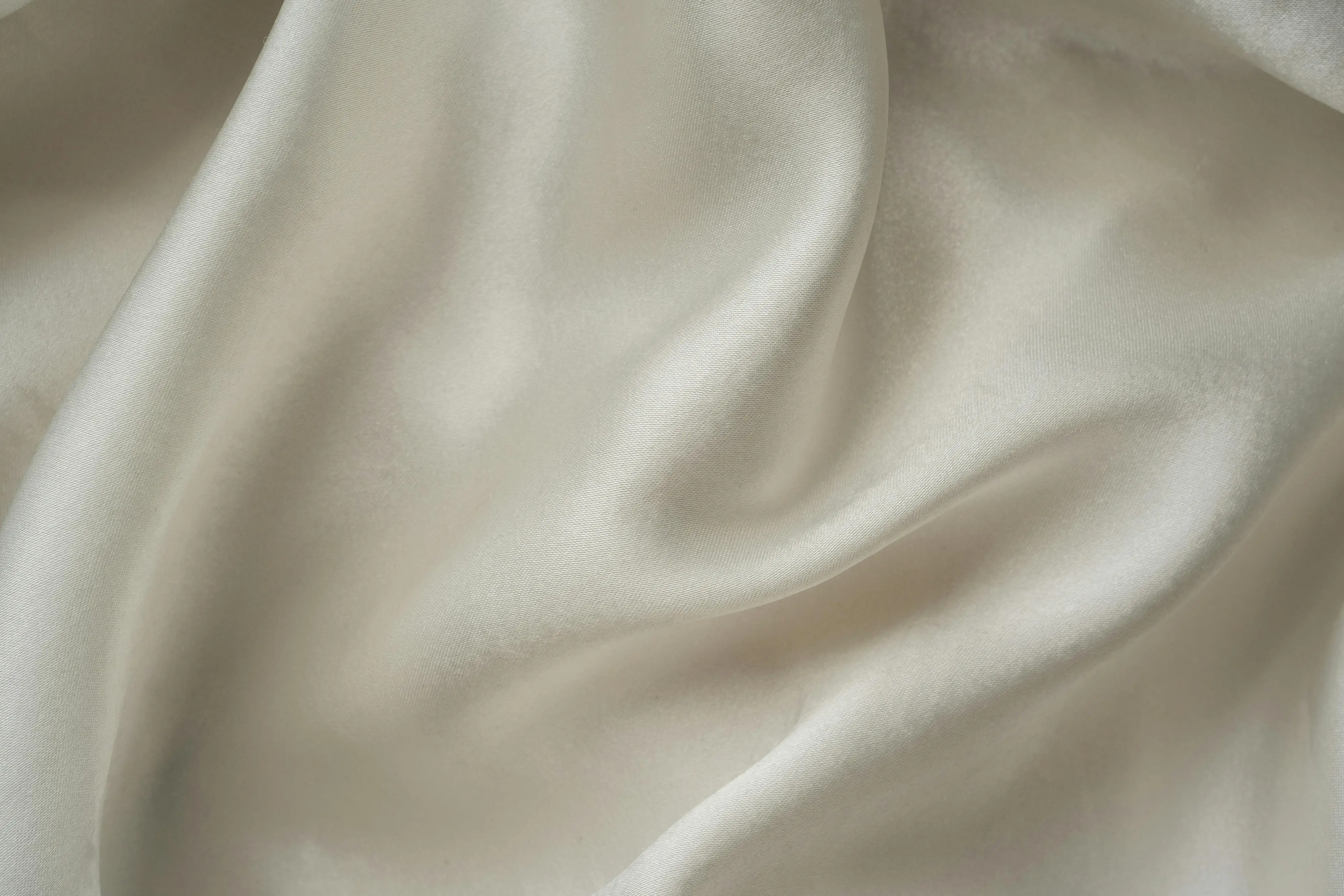 how to wash silk Close-up of smooth white silk fabric with soft folds and gentle draping.