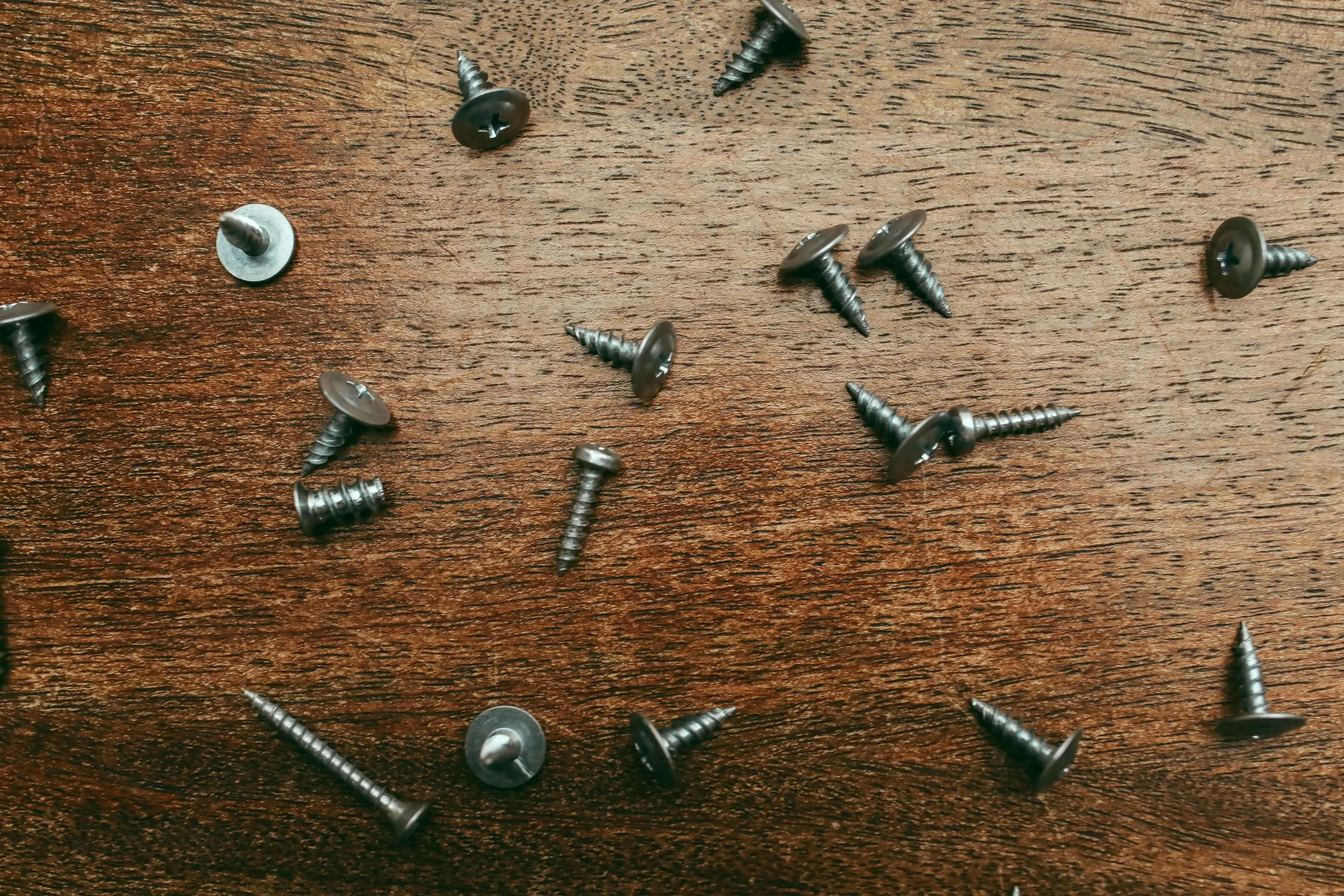 drywall screw dimensions A detailed view of scattered screws on a wooden table for repair or DIY projects.