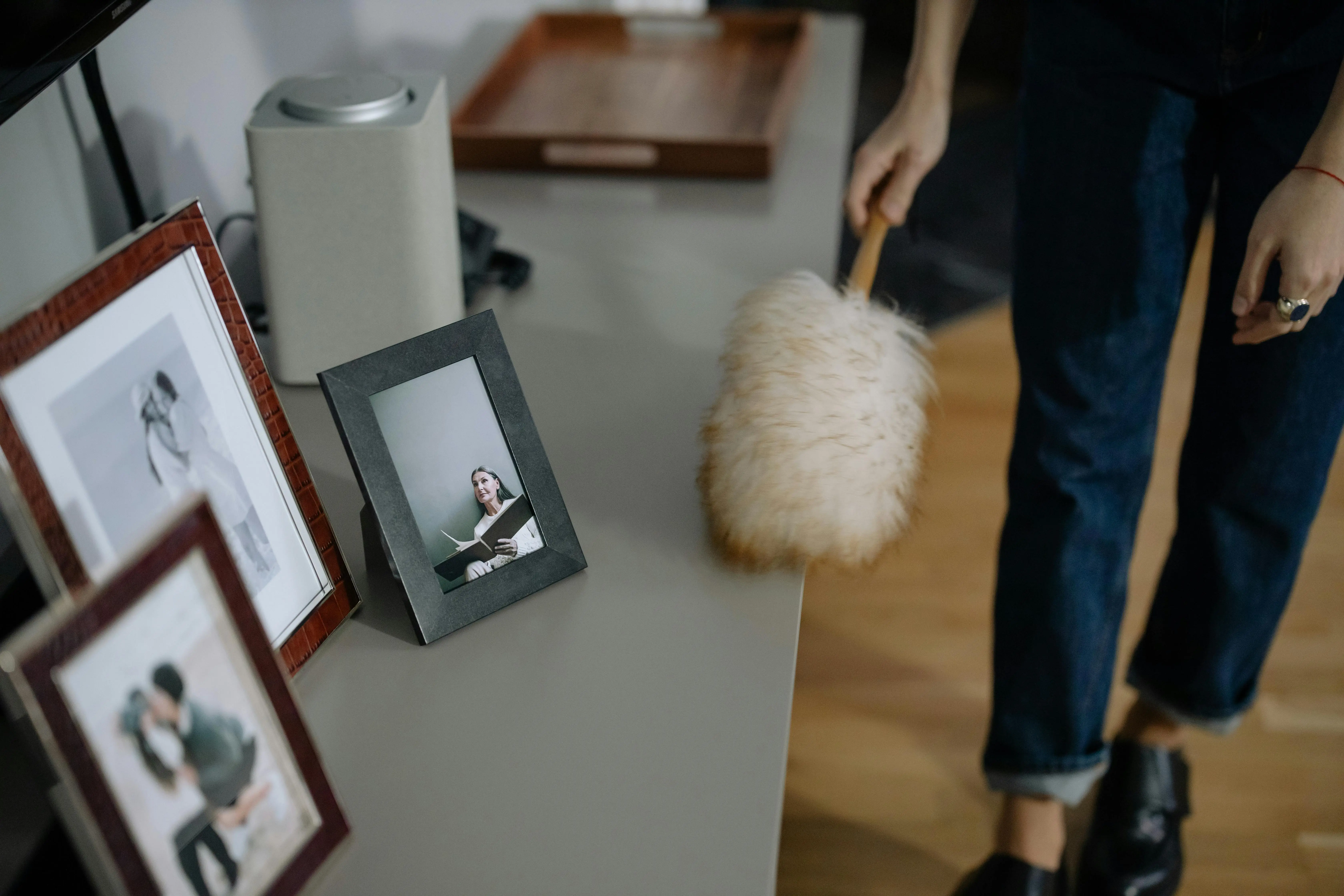 how to get rid of static electricity A woman using a feather duster to clean picture frames on shelves indoors.