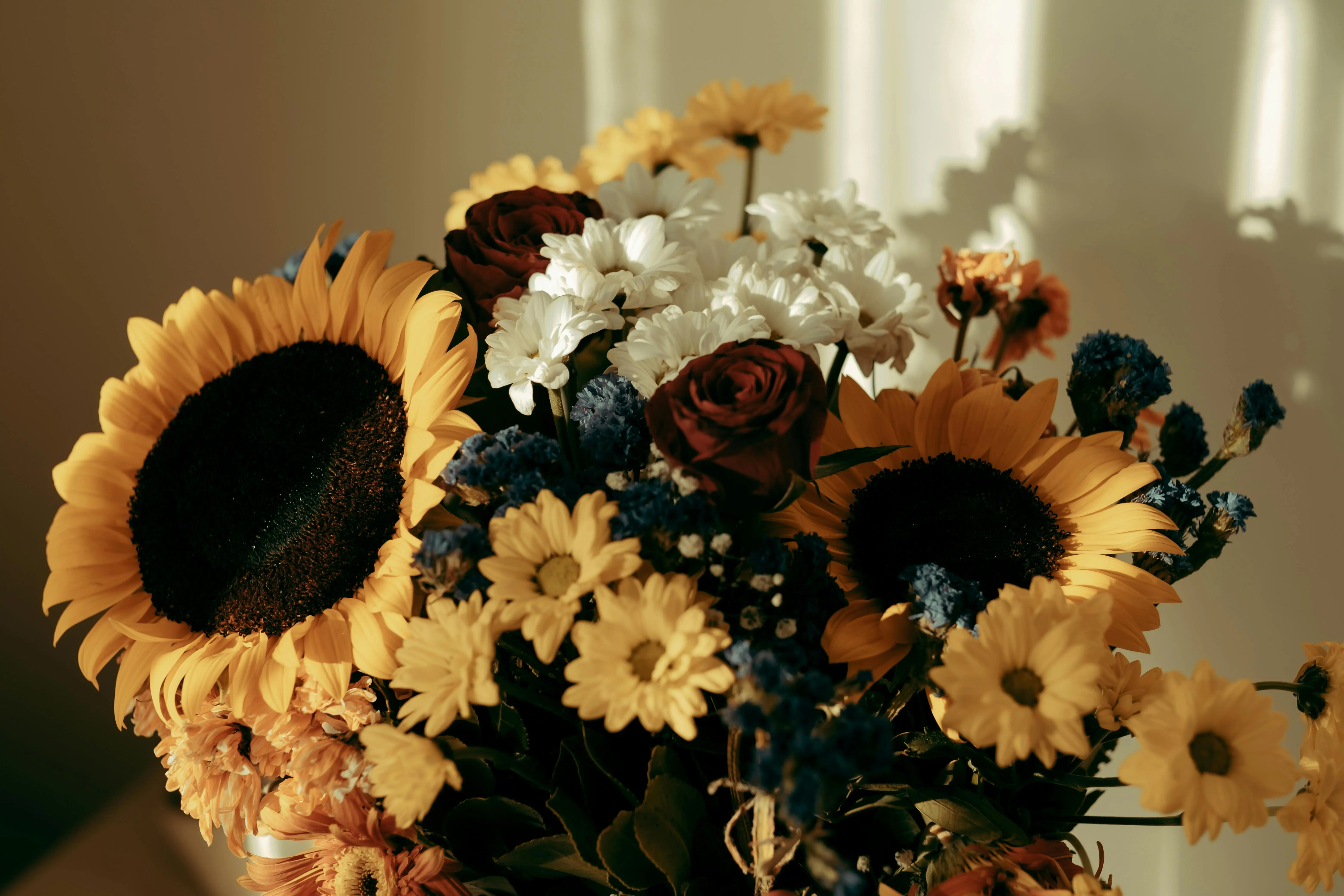sunflower and rose bouquet A stunning arrangement featuring sunflowers, roses, and daisies in warm lighting.
