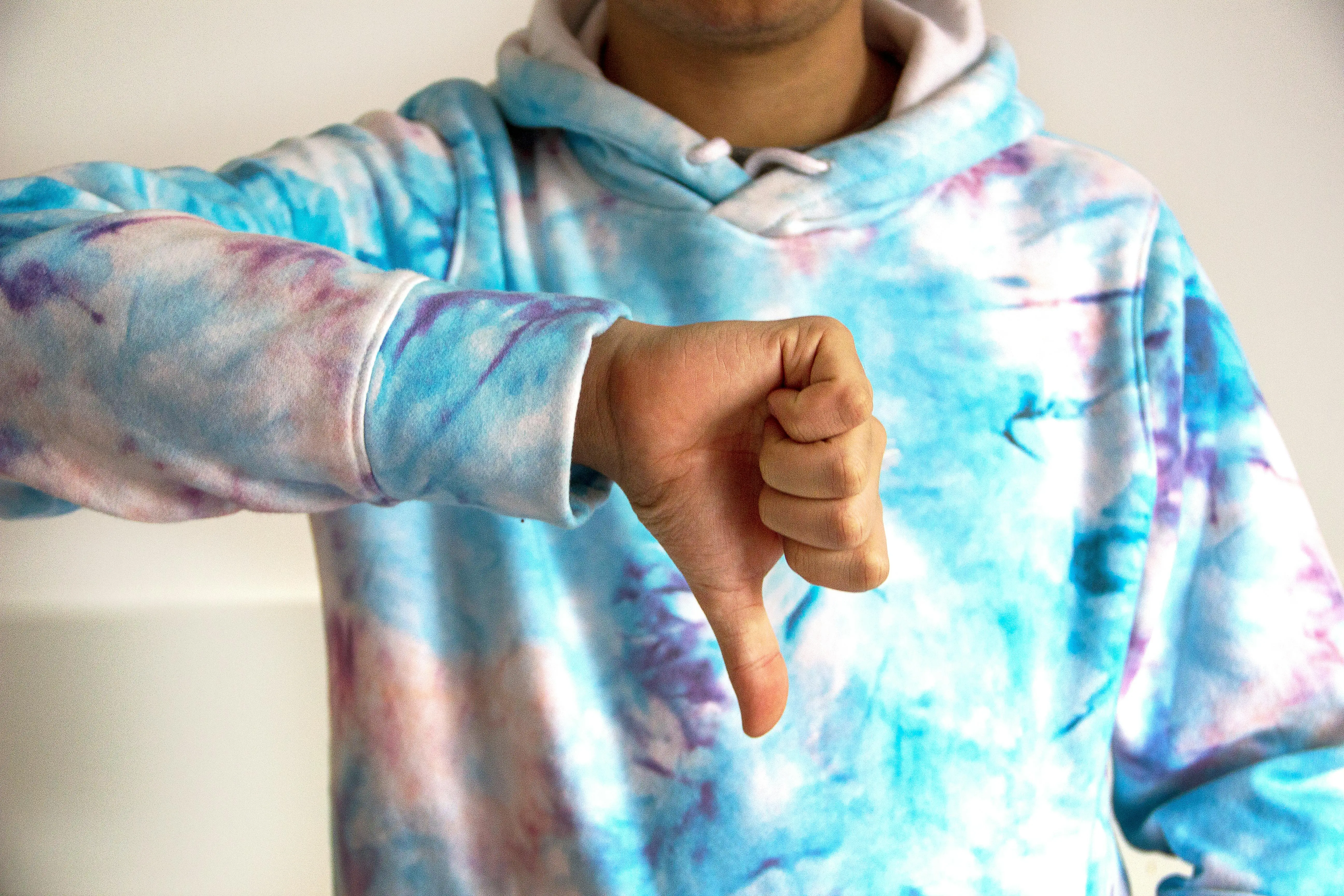blue tie dye shirt A person wearing a colorful tie-dye hoodie showing a thumbs down gesture, symbolizing disapproval.