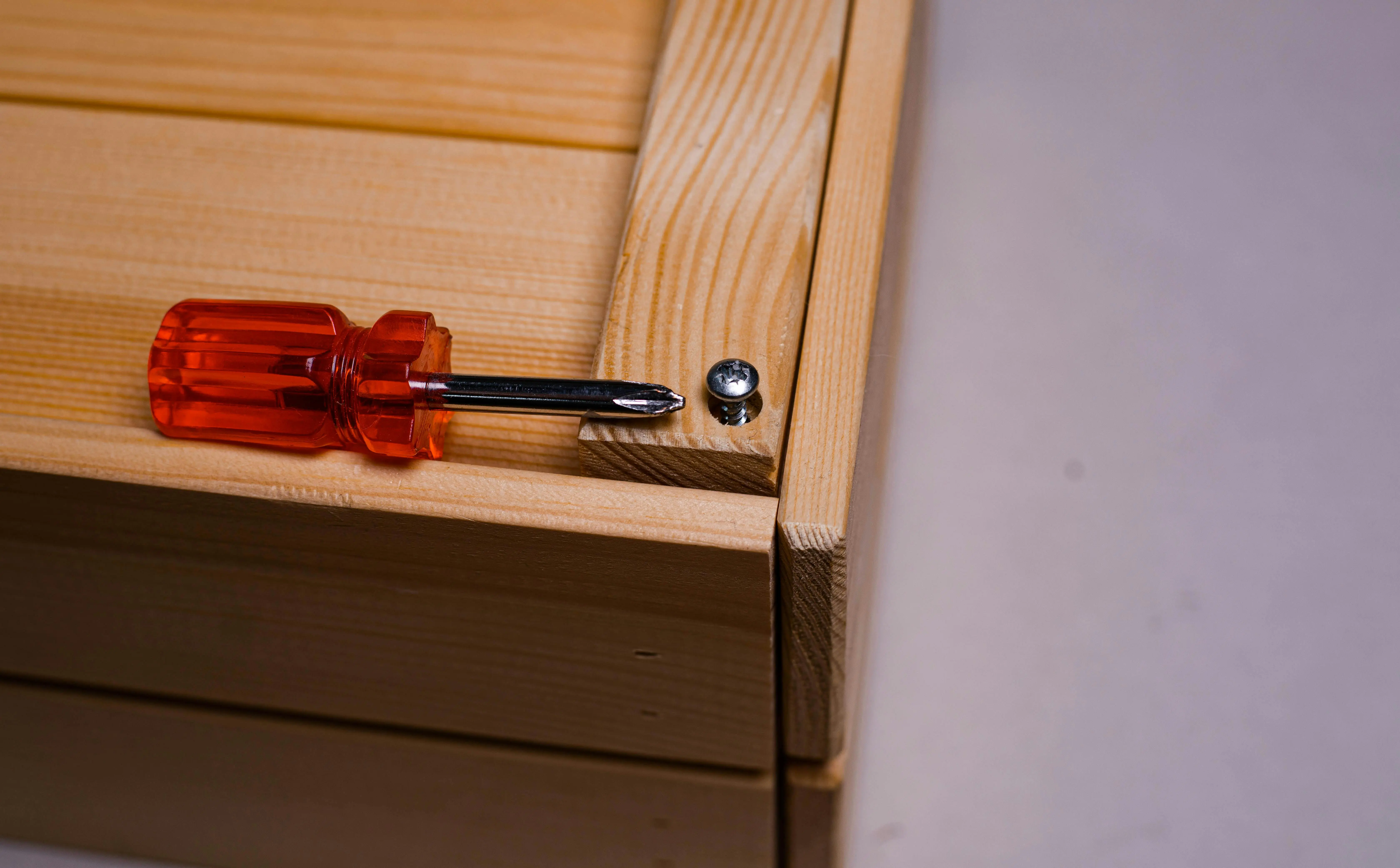 diy tool box A screwdriver beside a screw on a wooden box, depicting carpentry work.