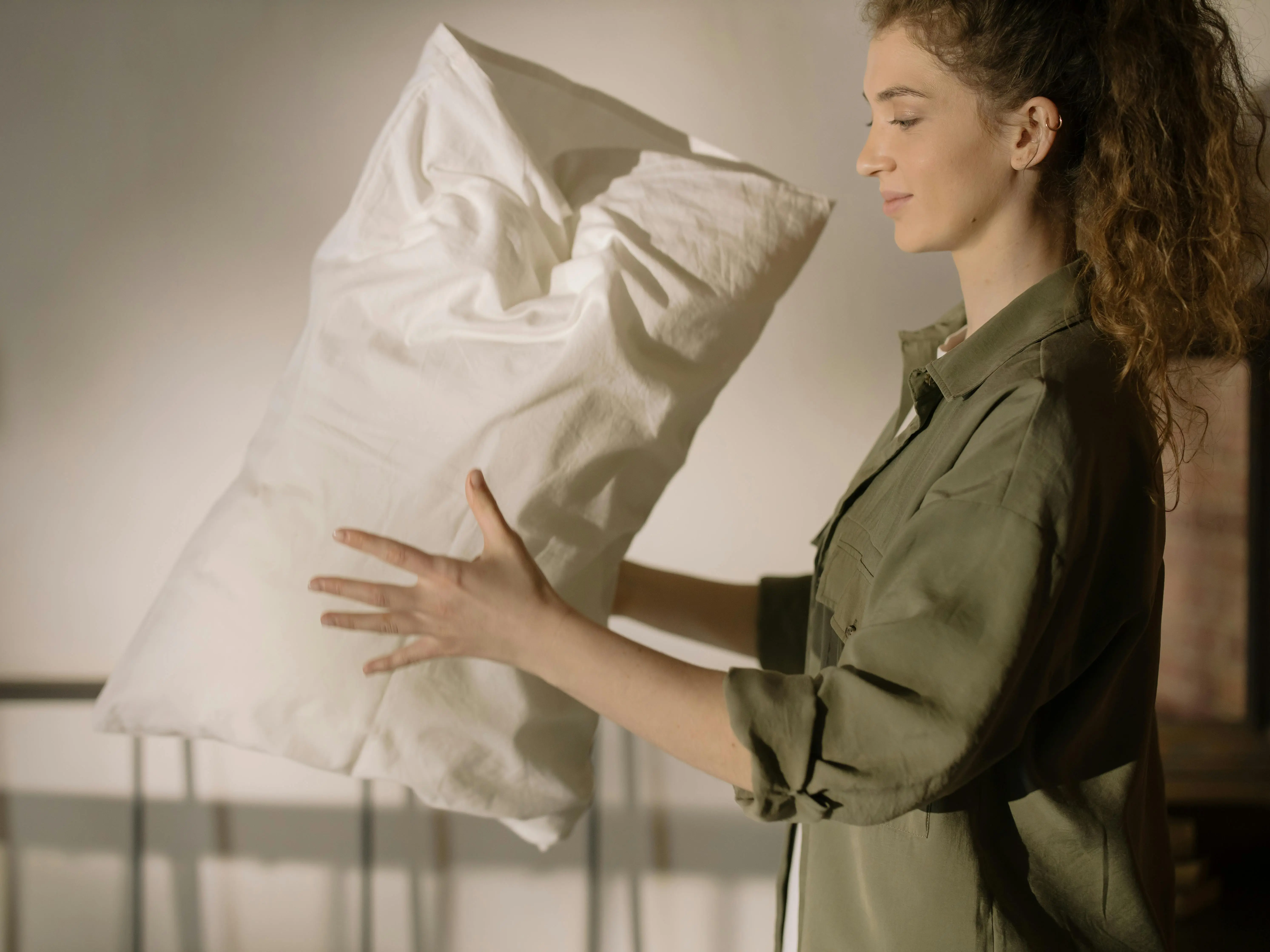 coastal decorative pillows A woman in a casual shirt fluffing a pillow in a cozy, well-lit bedroom.