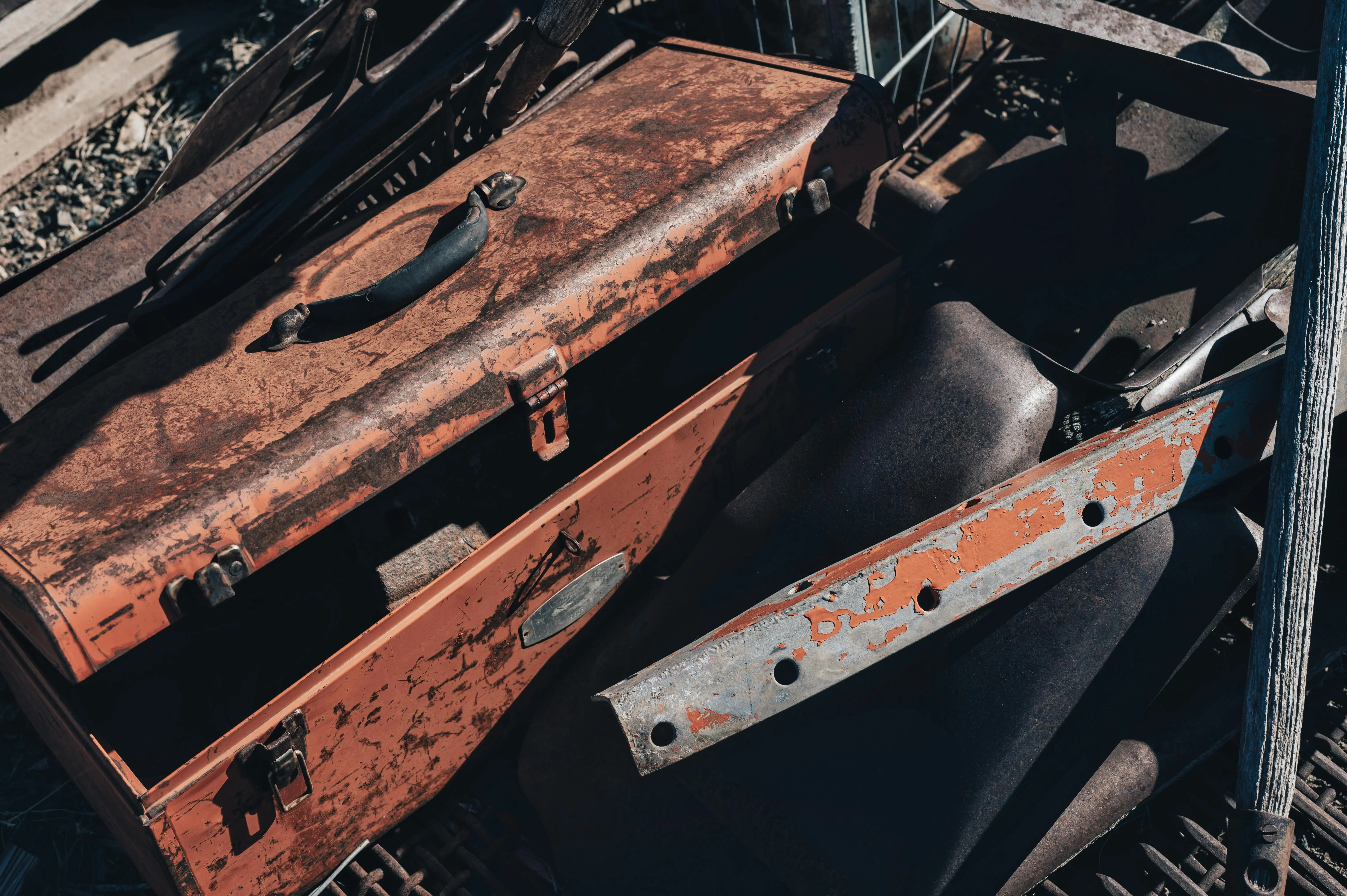 diy tool box A vintage rusty toolbox amidst scrap metal pieces in a junkyard under sunlight.