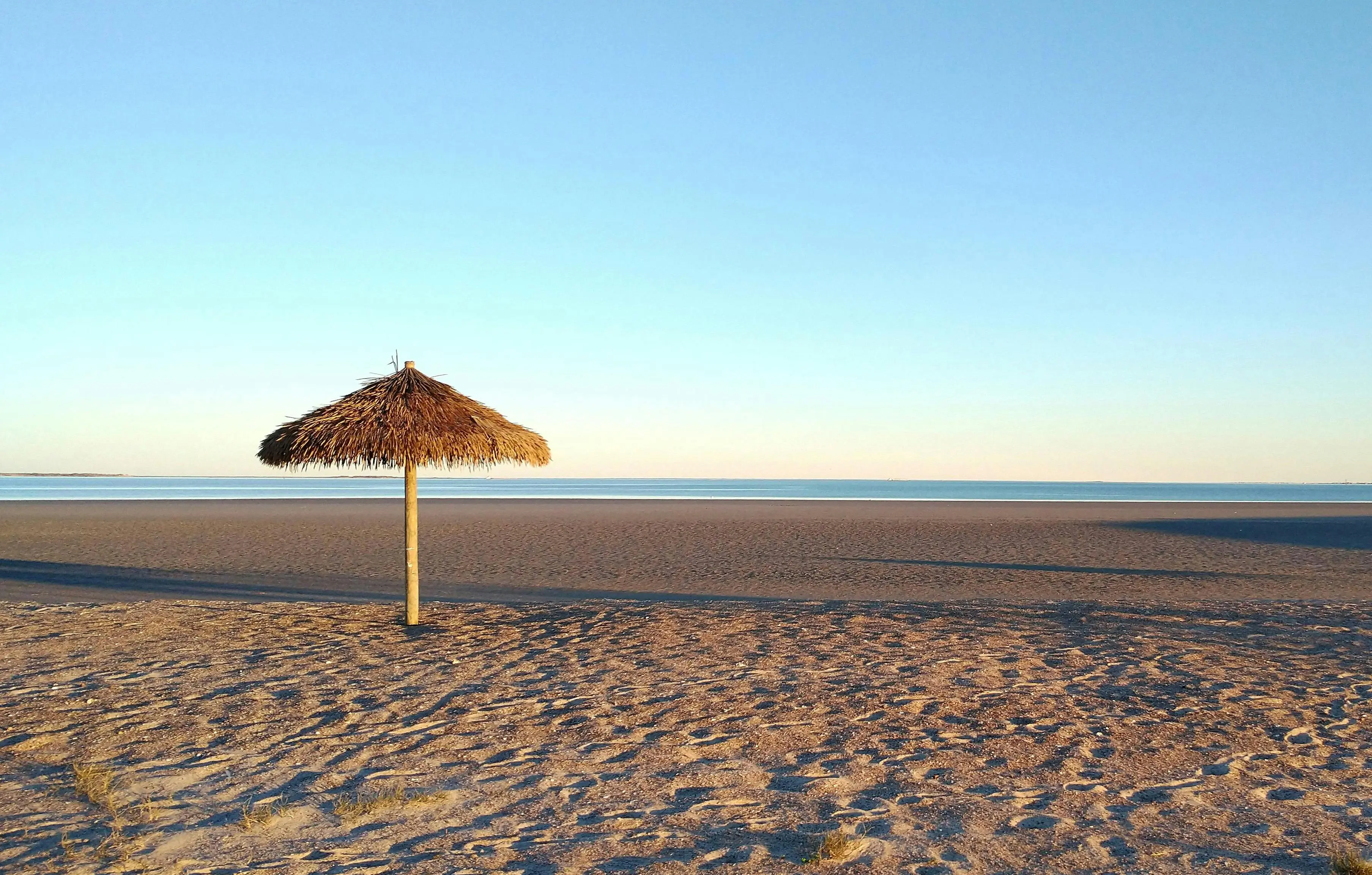 coastal chandelier Peaceful sandy beach in Port Lavaca, Texas with a straw hut under a clear blue sky.