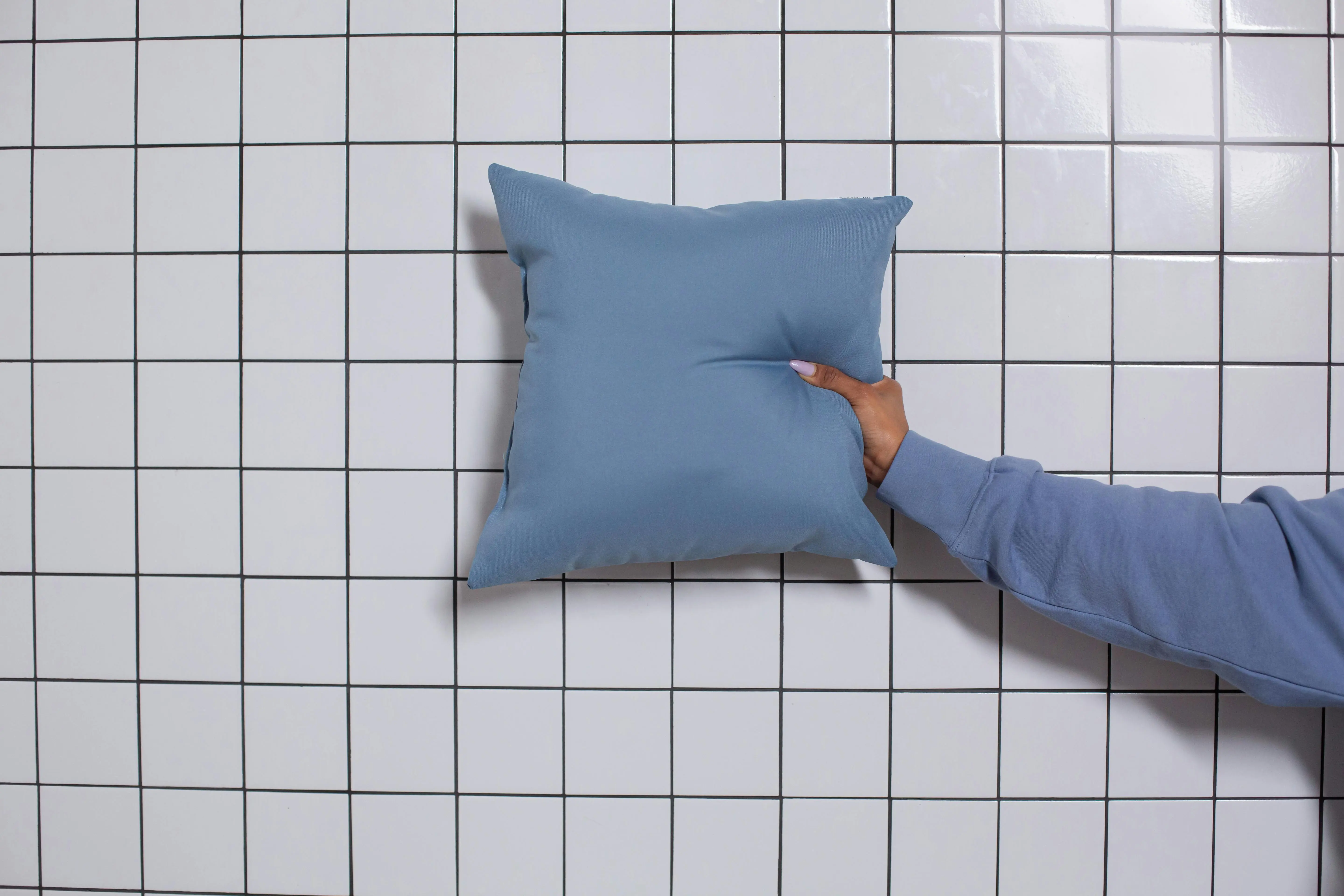 blue pillows Hand holding a blue cushion in front of a white tiled wall, minimal aesthetic