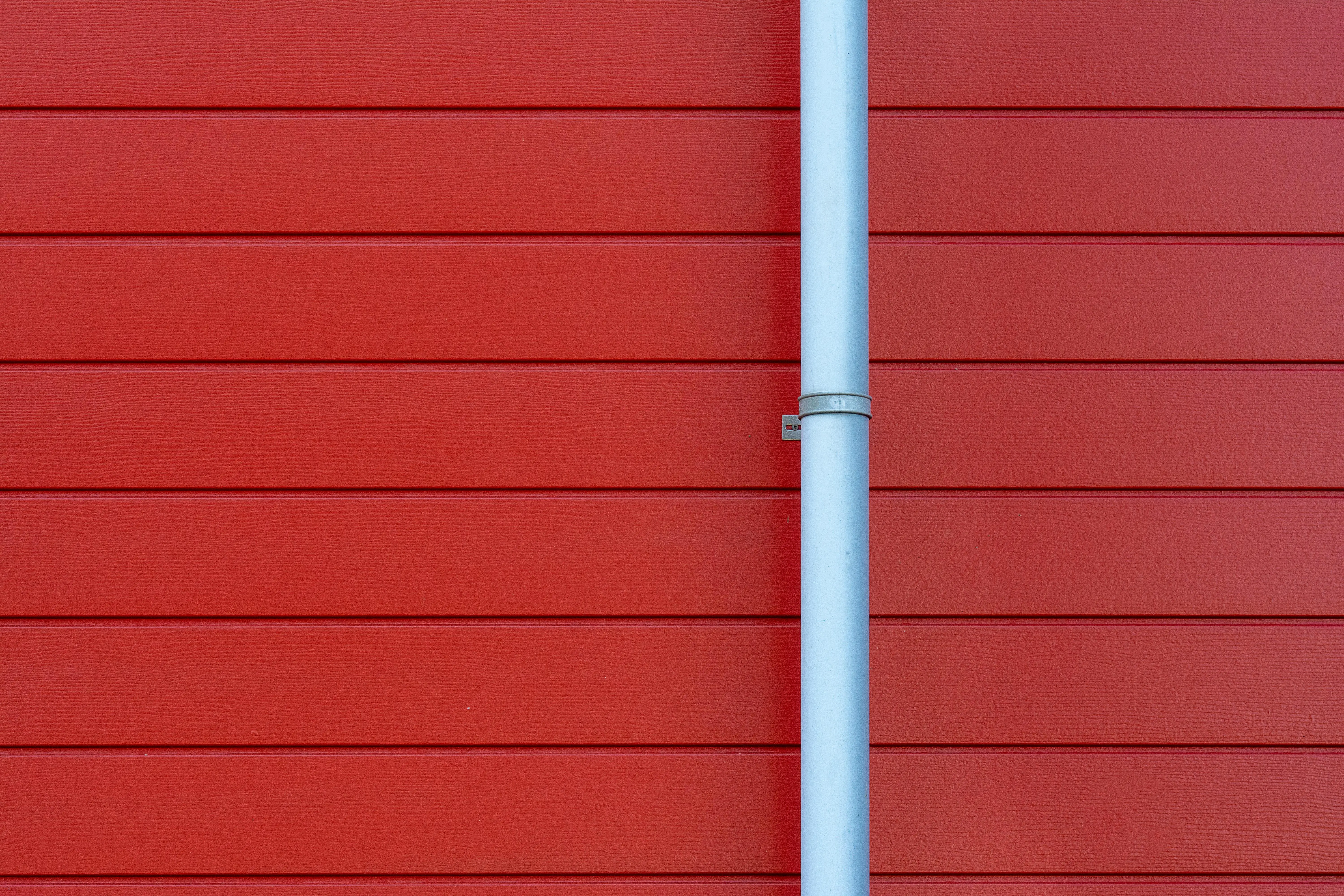dark blue siding colors A minimalist photo of a red wall with a white rain gutter, showing clean lines and vibrant color contrast.