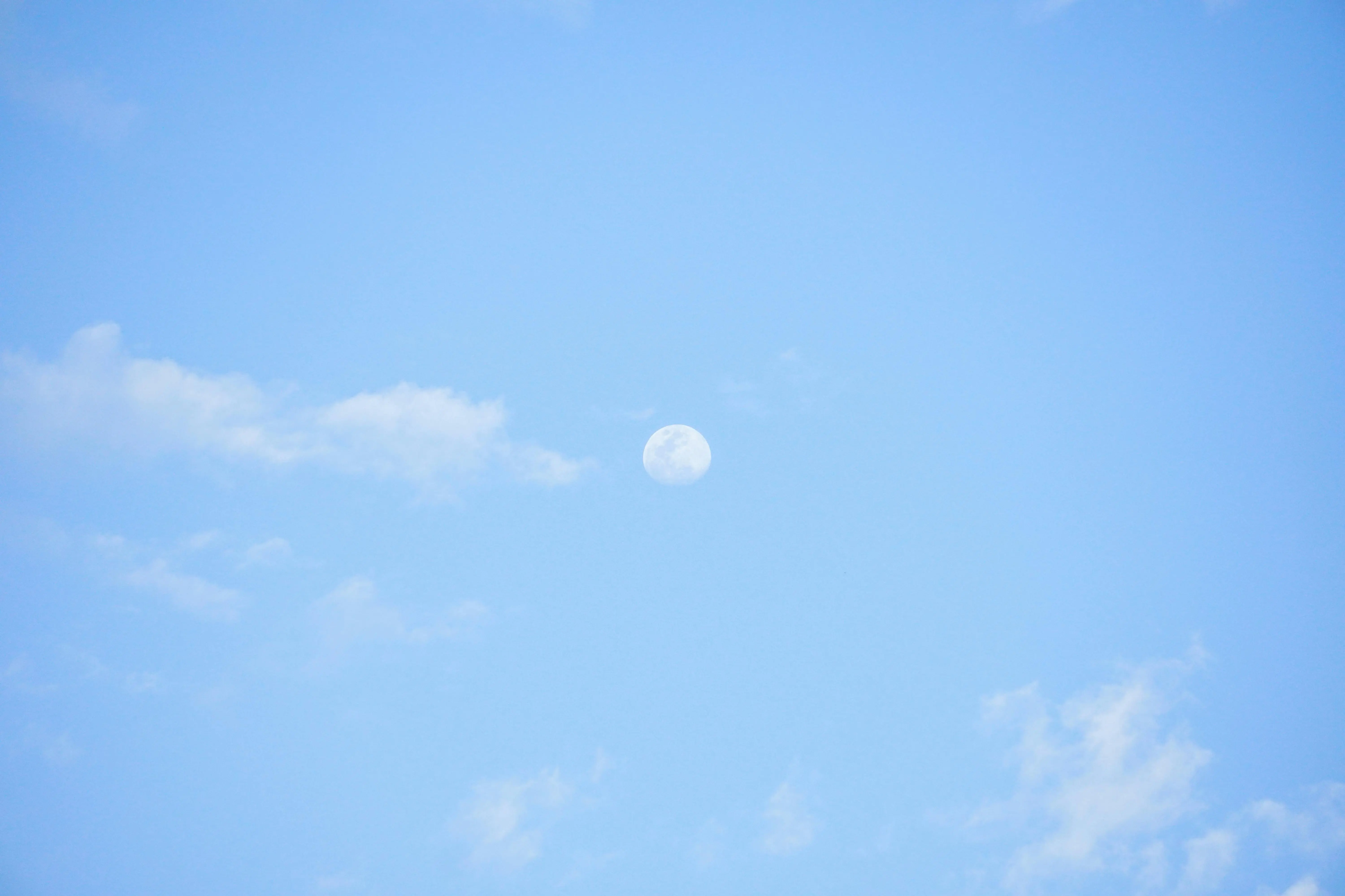 blue and white pillows A serene blue sky with the moon visible amidst light white clouds during the day.