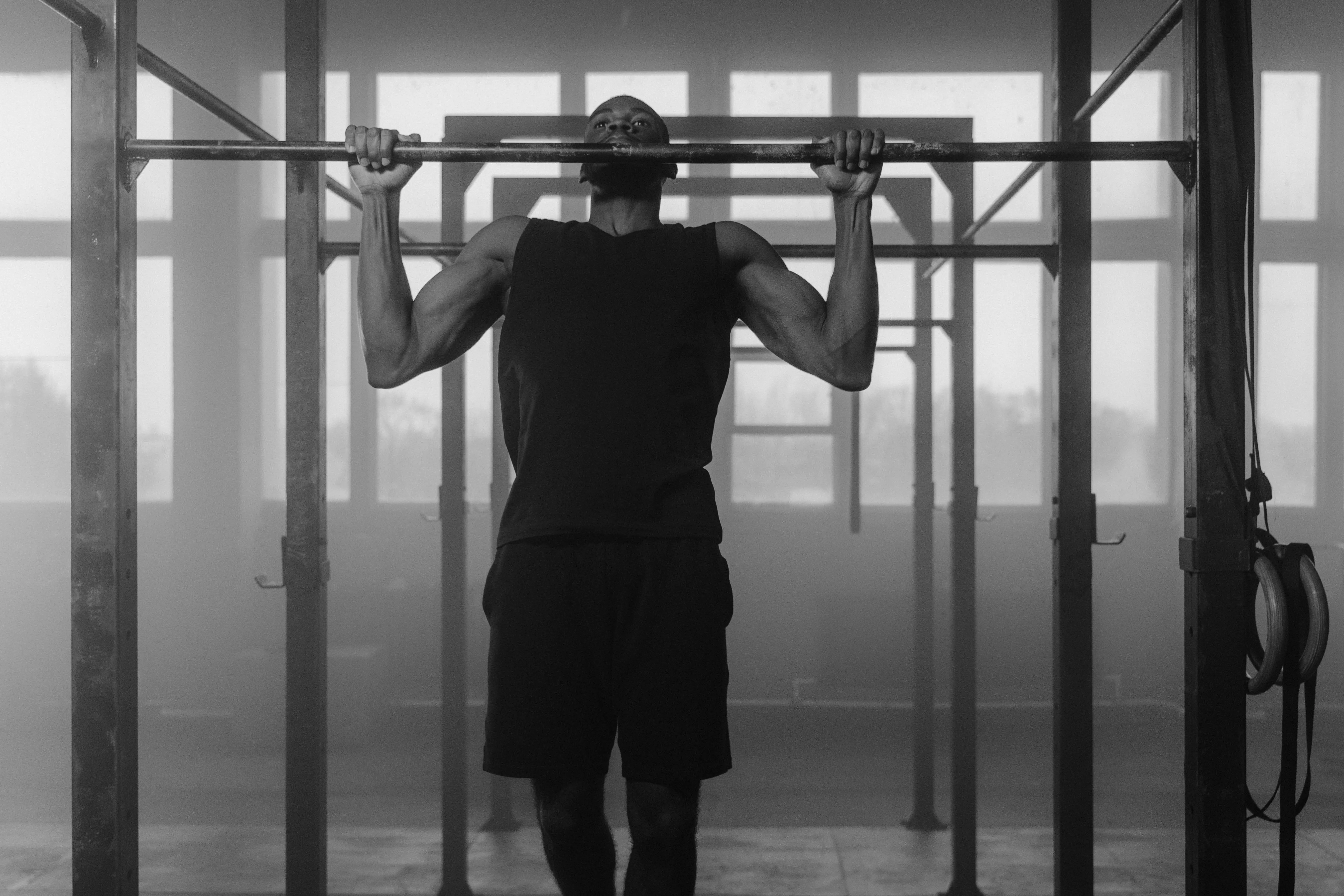 black drawer pulls Black and white photo of a man performing pull-ups in an indoor gym setting, showcasing strength and fitness.