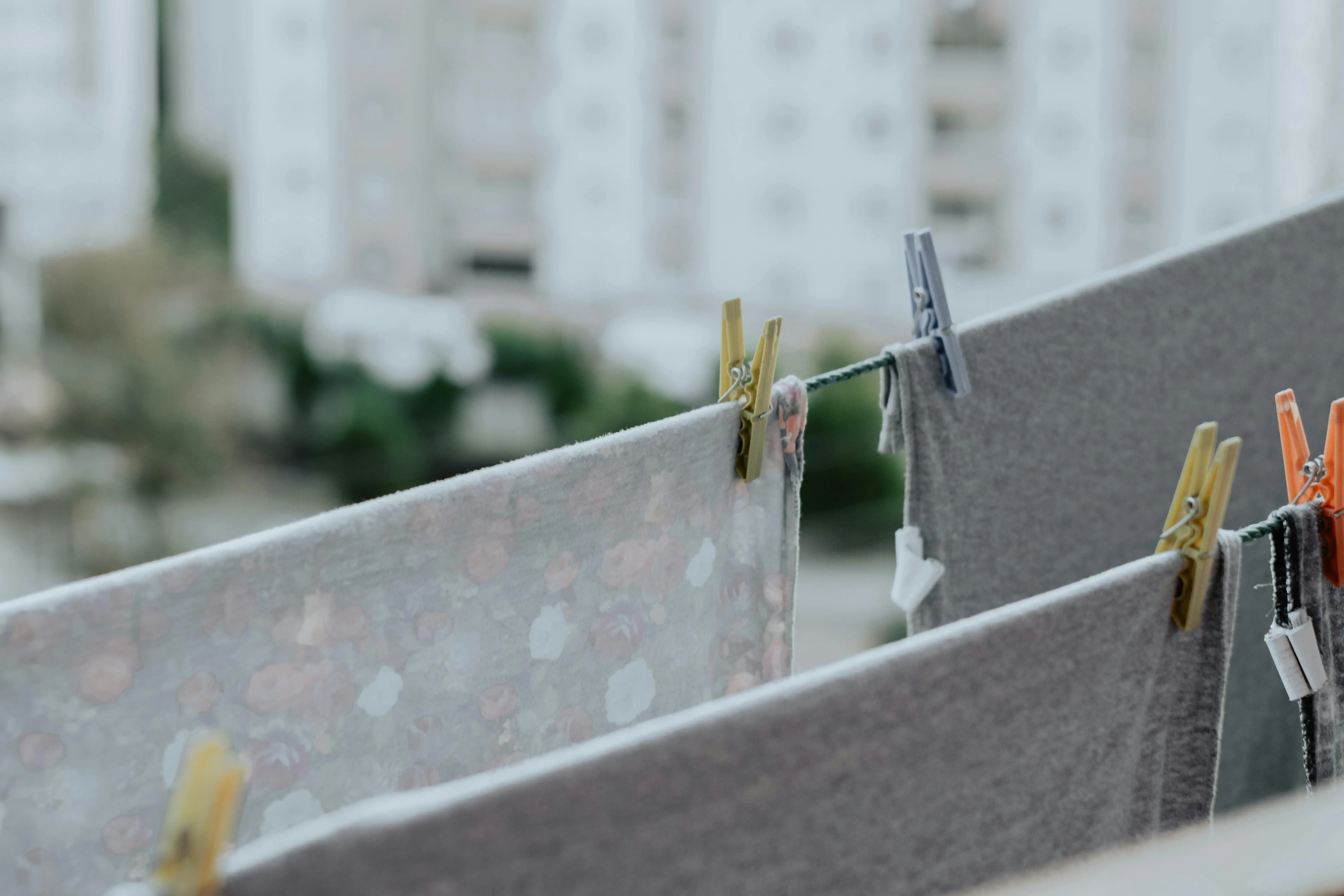 how to wash 100 cotton Colorful laundry hanging on a balcony with blurred urban buildings in the background.