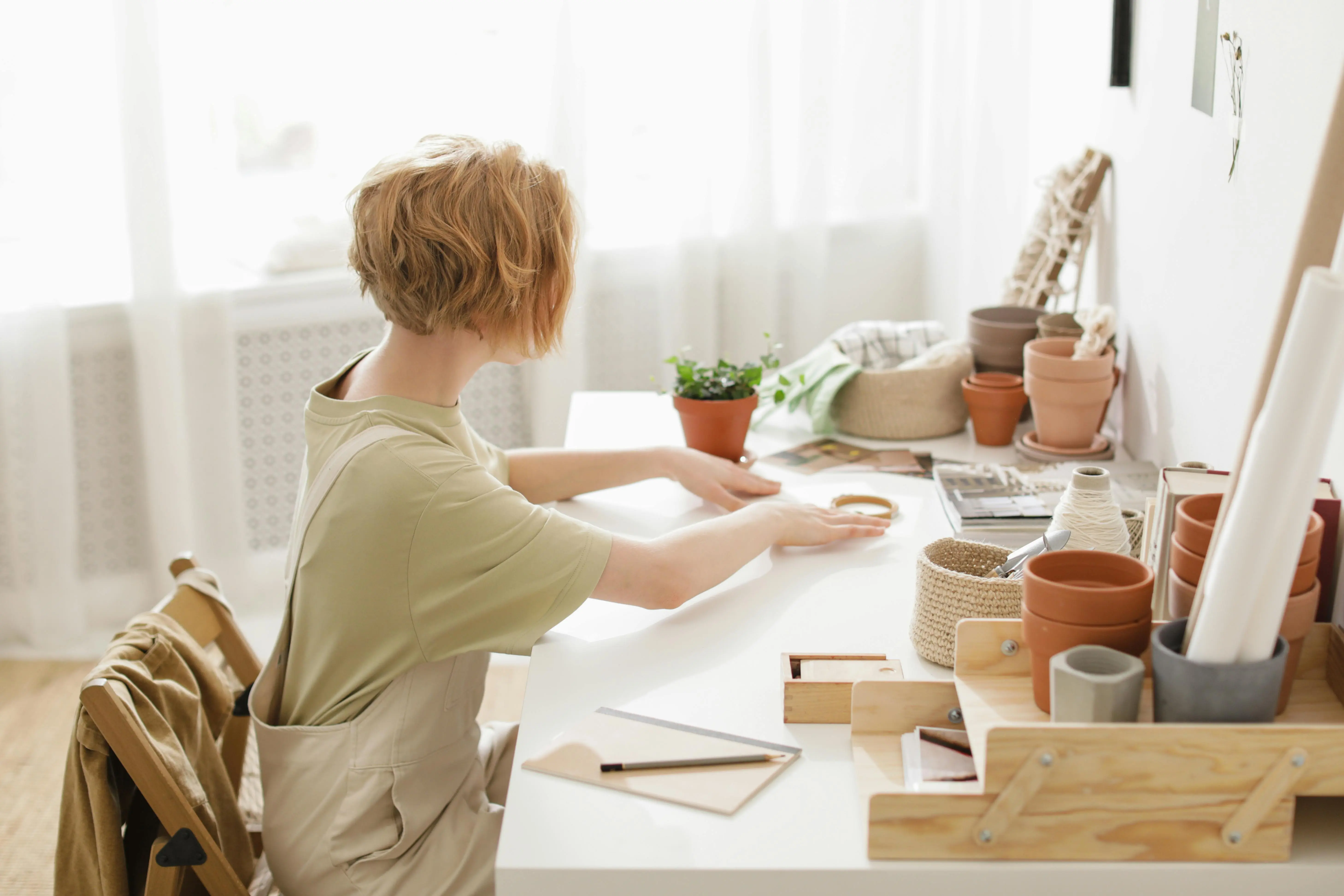 diy small craft room ideas A woman sits in a cozy workspace crafting with flower pots and supplies.