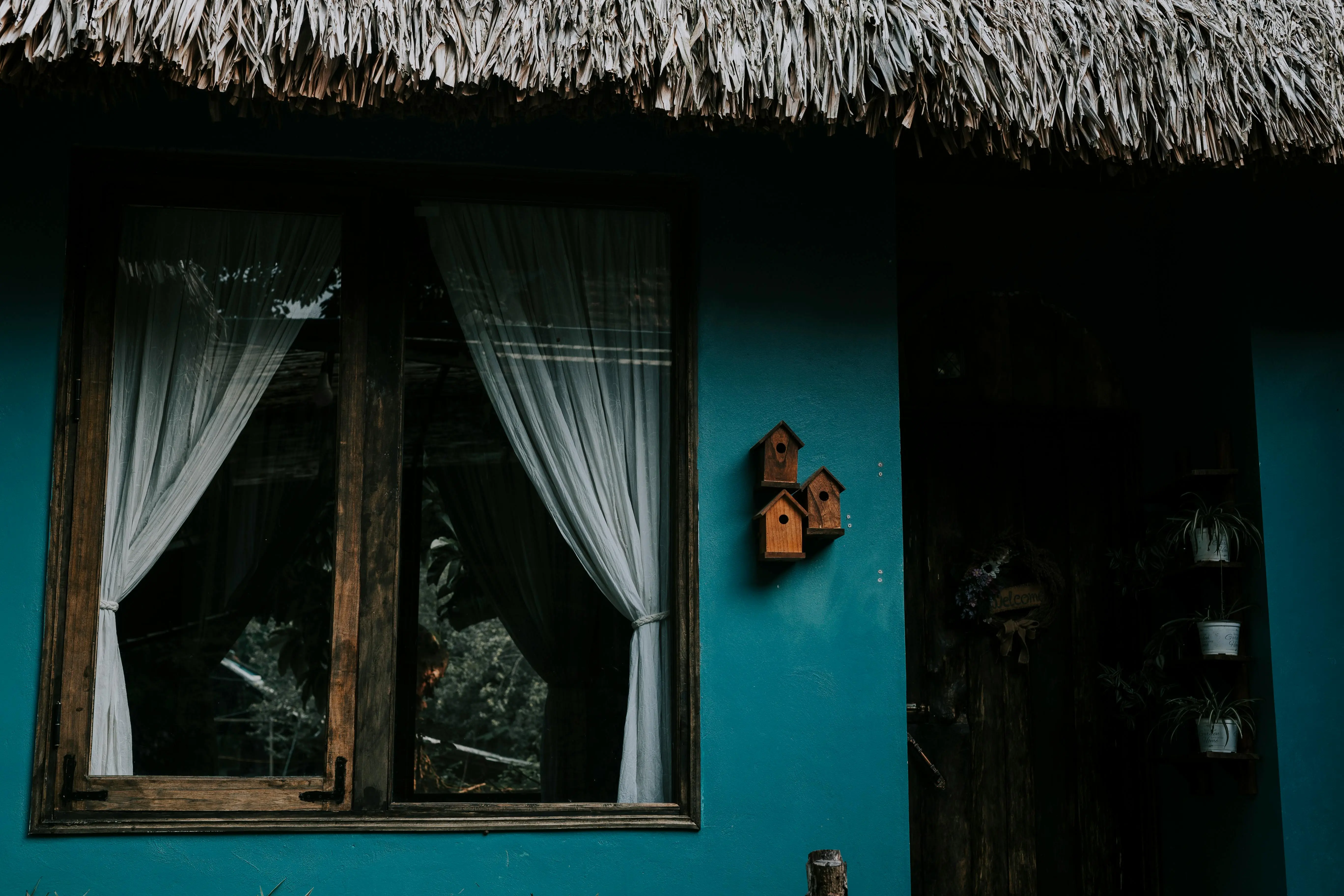 dark blue siding colors An inviting blue house facade with birdhouses, curtains, and a nipa roof for a nature-inspired look.