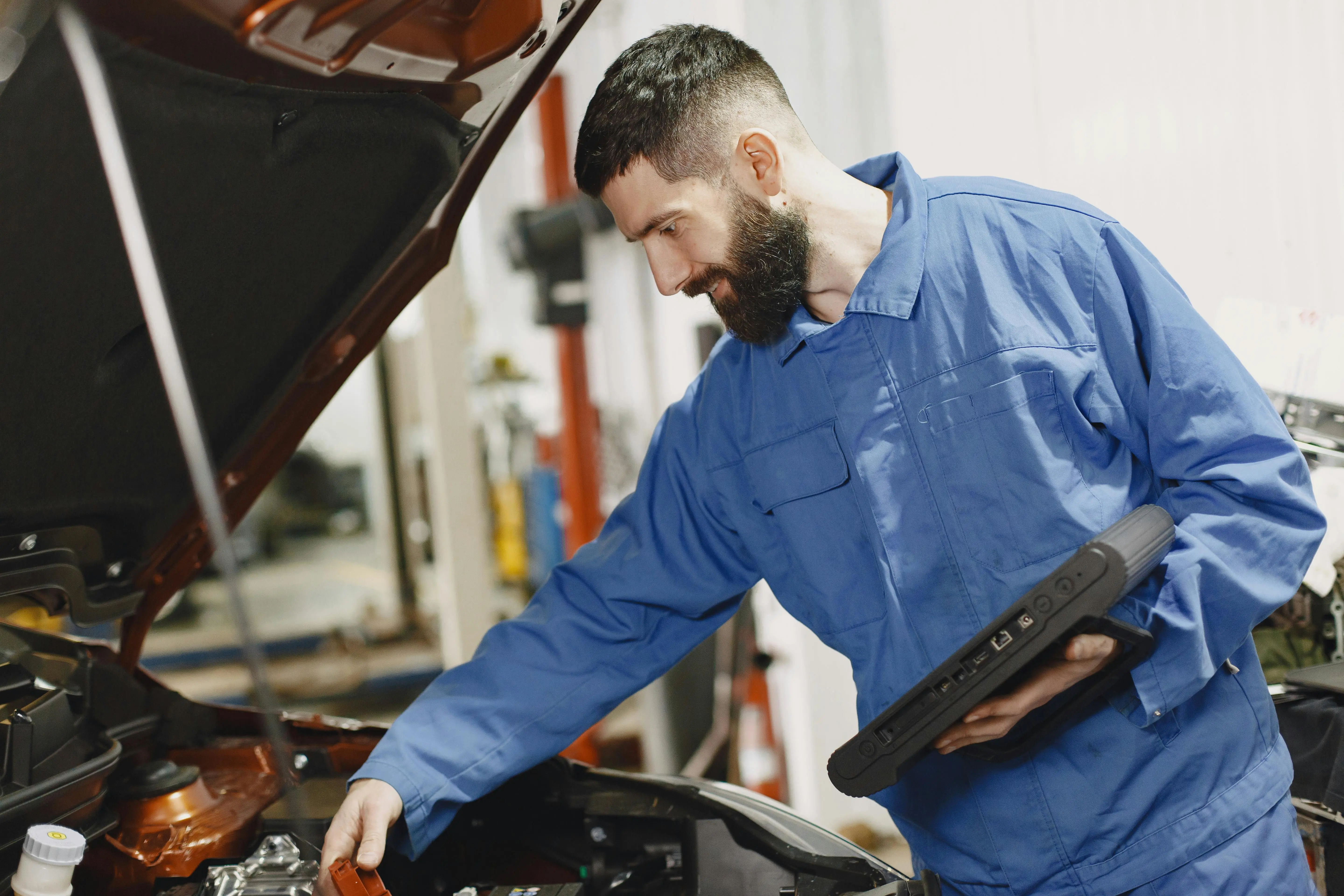 commercial clothes dryer An auto mechanic in blue coveralls inspecting a car's engine in a garage.