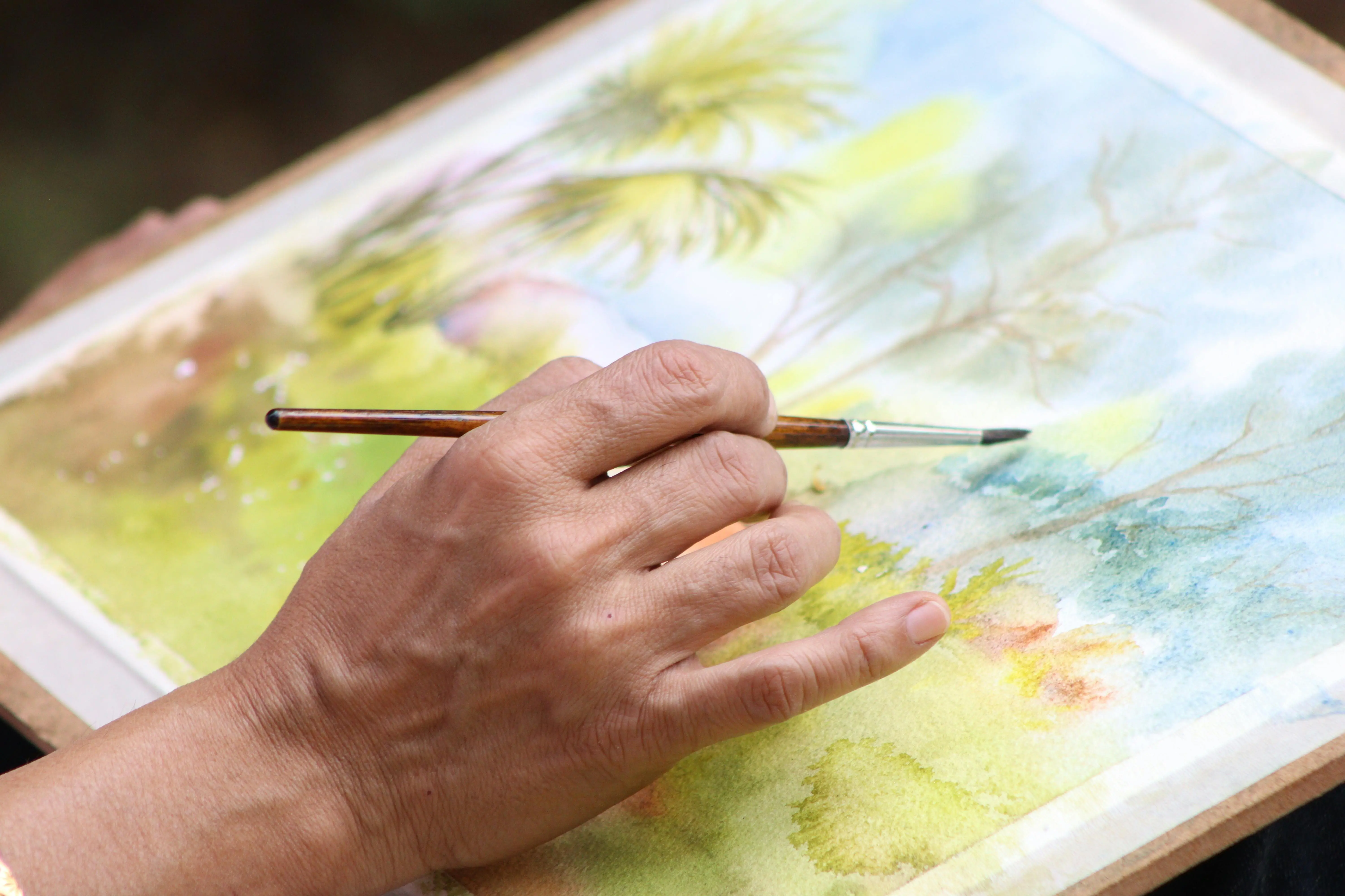 watercolour painting kit Close-up view of a hand painting a vibrant watercolor landscape. Artistic expression captured.