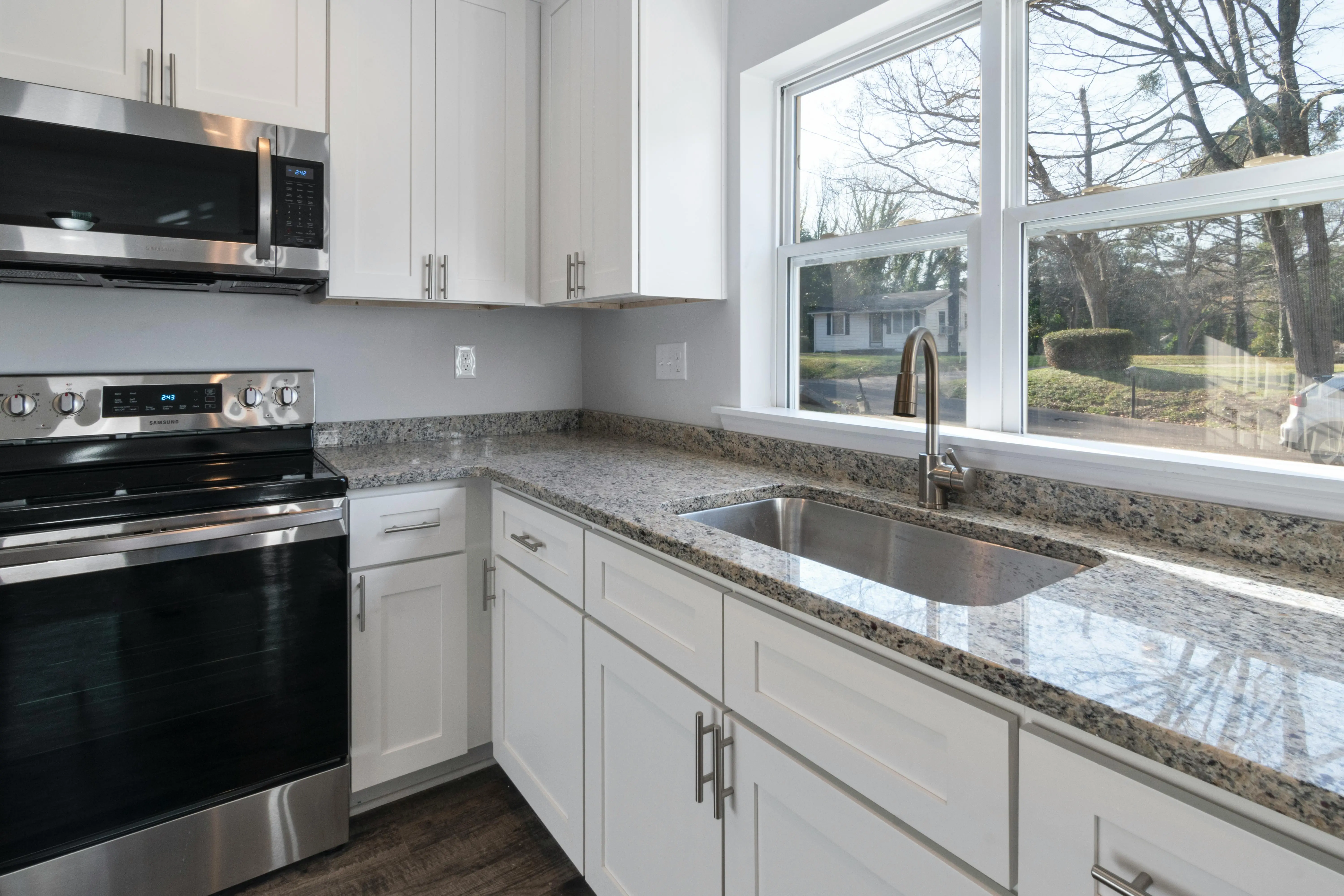 grey granite countertops colors Bright kitchen showcasing granite countertops, stainless steel appliances, and large windows.
