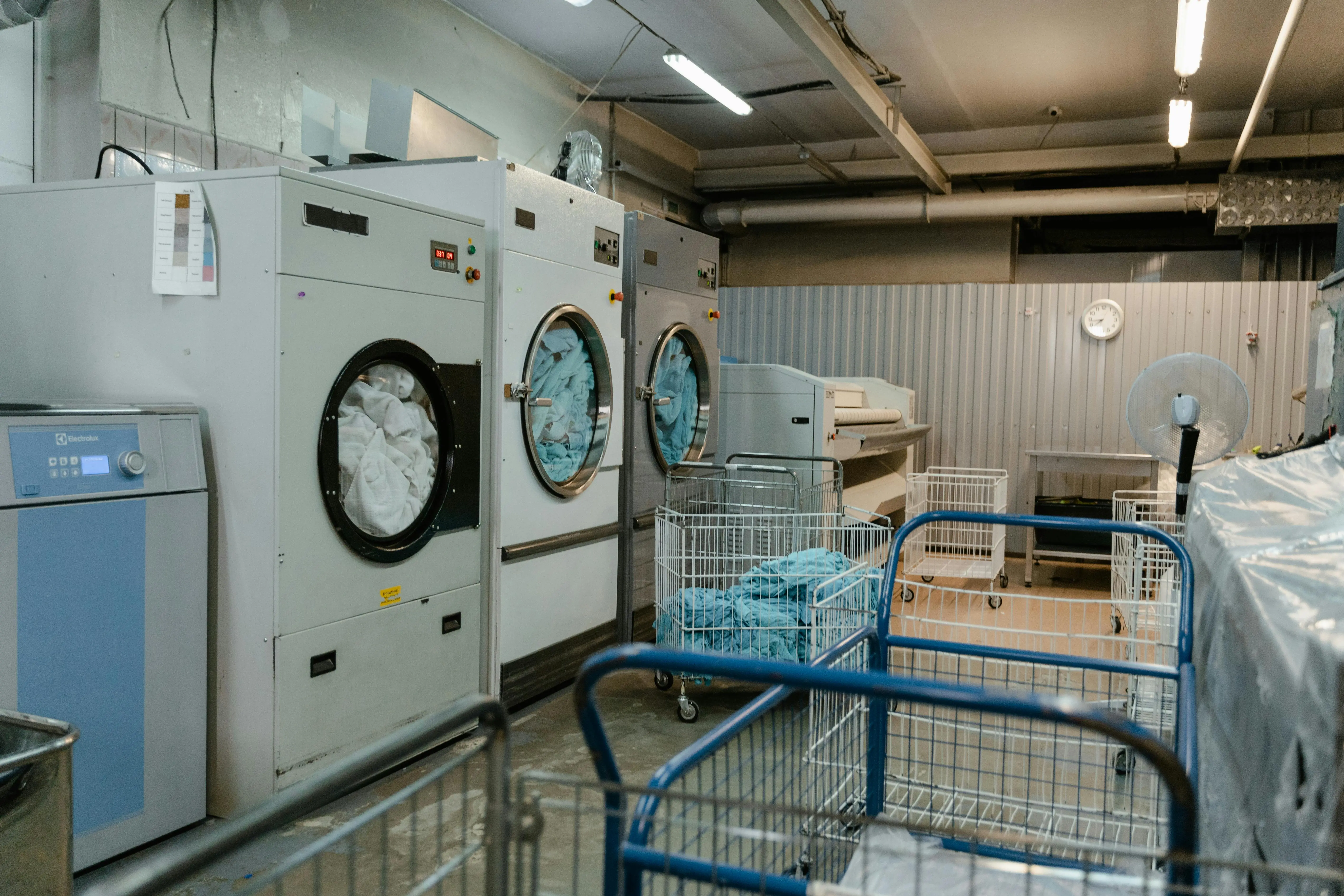 how much does a dryer weigh Interior view of an industrial laundry room with washers and rolling carts.