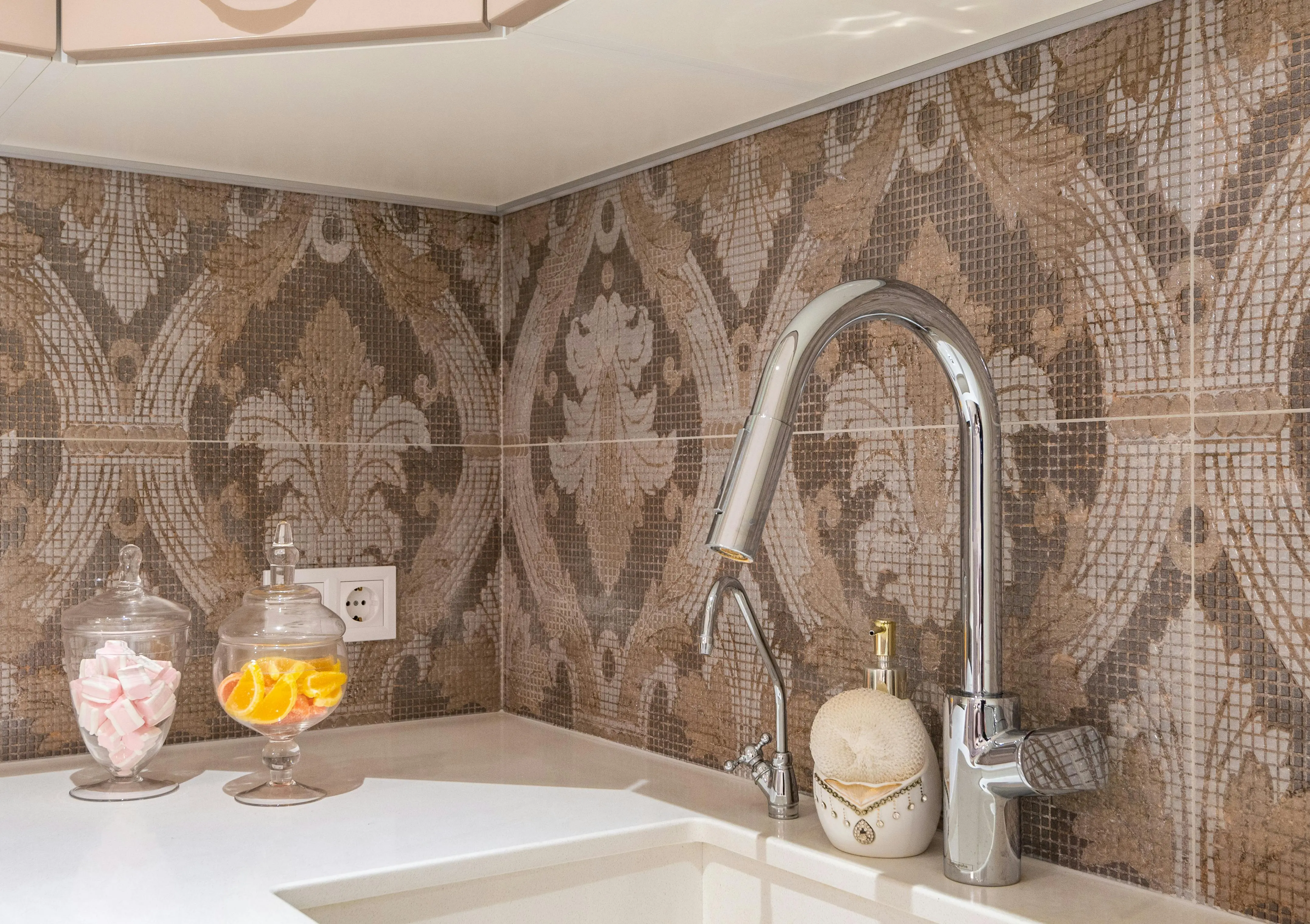 floral tile backsplash Contemporary kitchen stone counter with undercounter sink and shiny metal faucets at beige and brown tiled backsplash with ornament