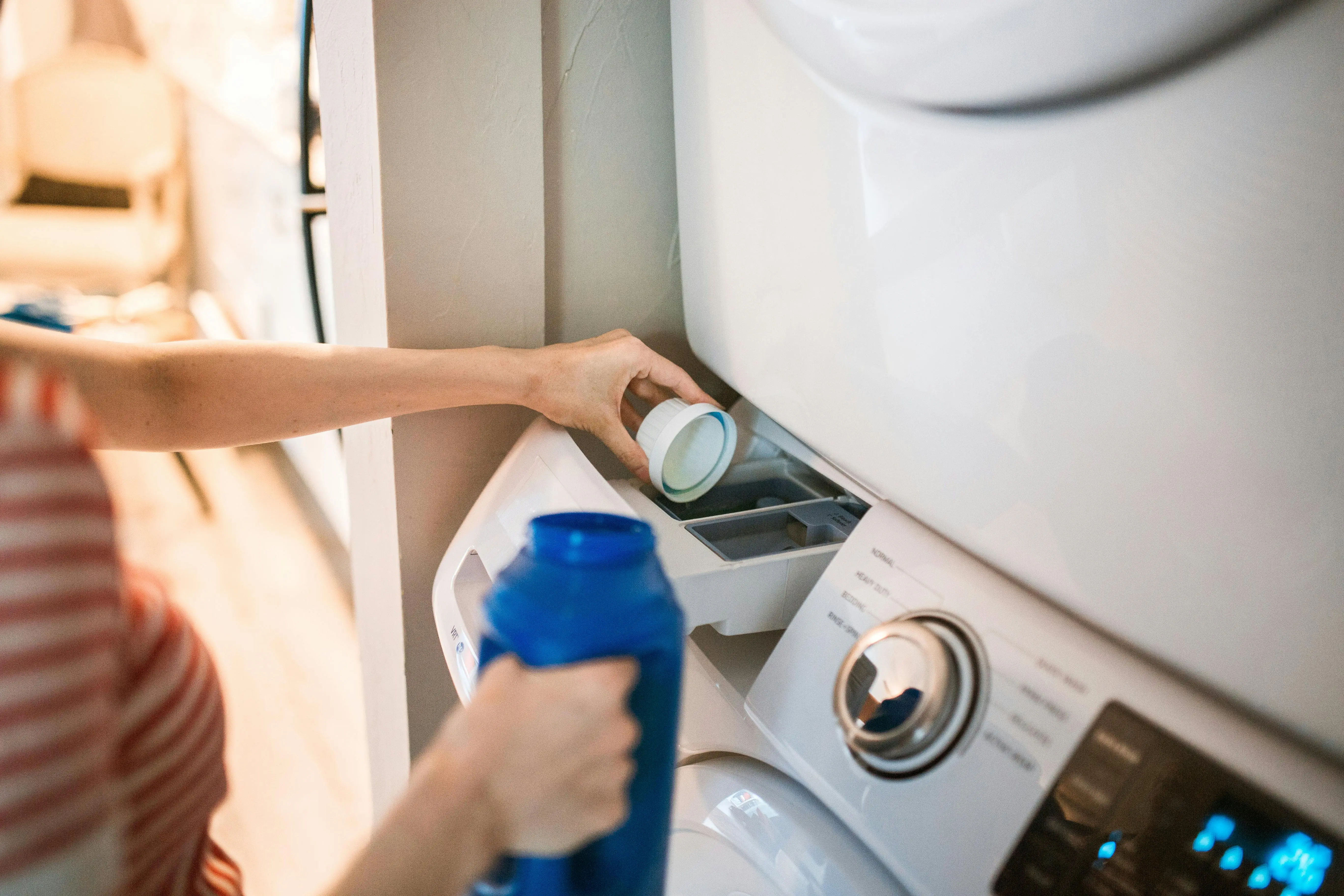 fragrance free laundry detergent Close-up of a person pouring detergent into a front-loading washer, emphasizing household chores.