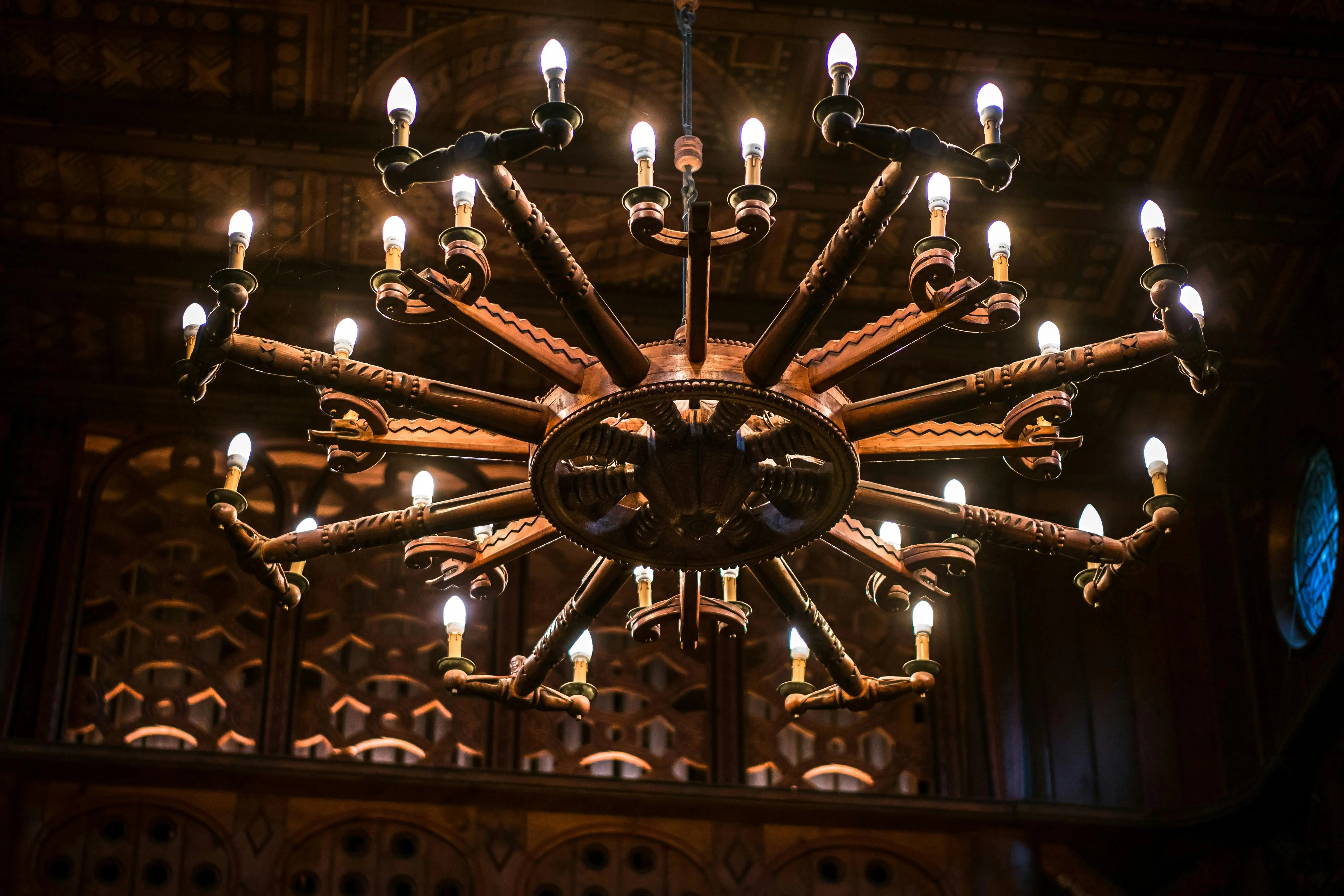 exclusive opulent interior designs Elegant wooden chandelier with illuminated bulbs, showcasing intricate designs in a vintage setting.