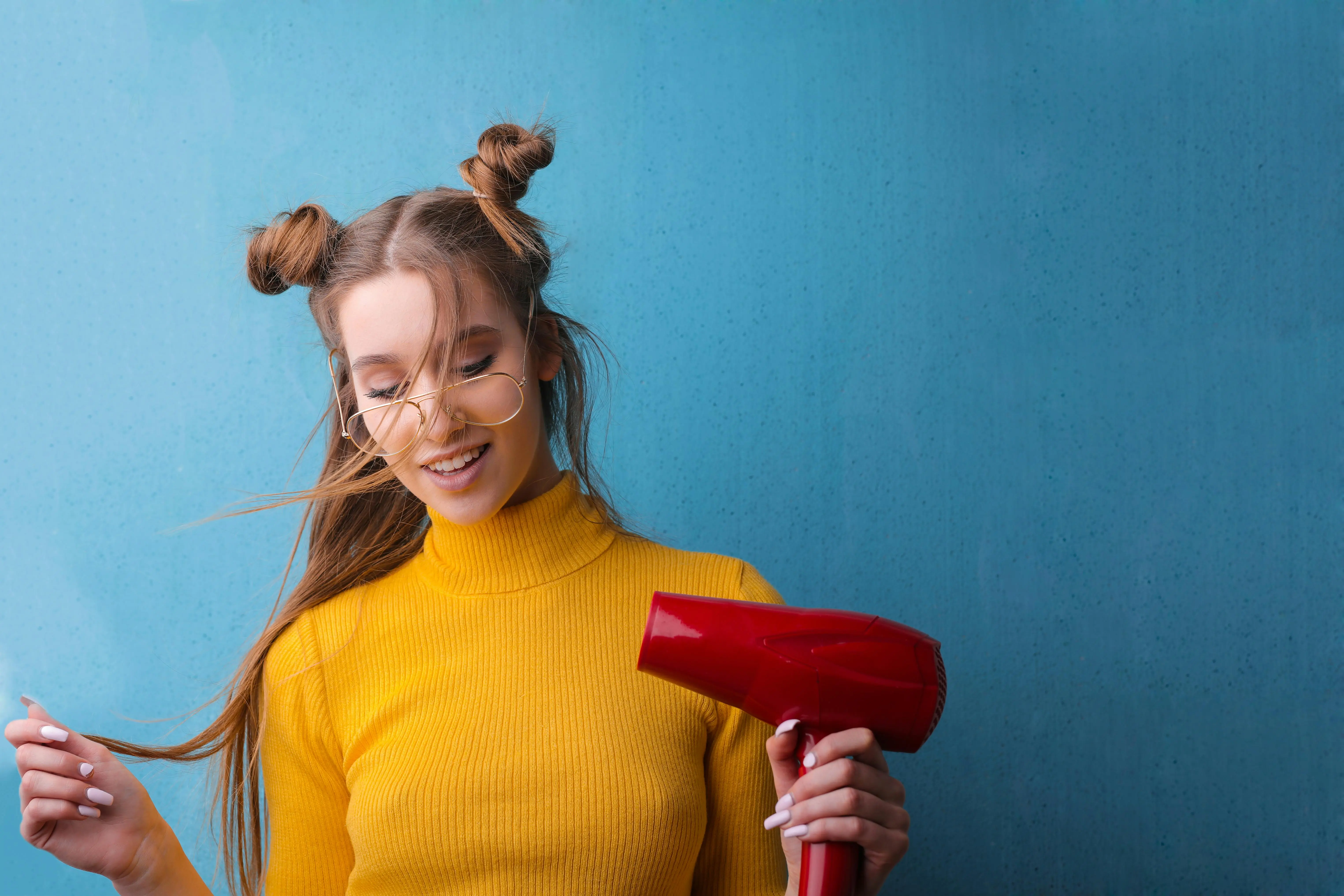 how much does a dryer weigh Woman with quirky hairstyle and glasses smiling with a hair dryer against a blue background.